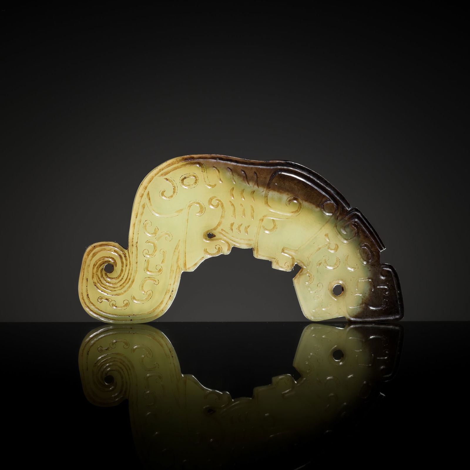 A RARE DARK GREEN AND BROWN JADE 'TIGER' PENDANT, SPRING AND AUTUMN PERIOD: A RARE DARK GREEN AND BROWN JADE 'TIGER' PENDANT, SPRING AND AUTUMN PERIOD China, 770-475 BC. Of flattened form, carved as a stylized crouching tiger, its body, finely incised with scrollwork and lin