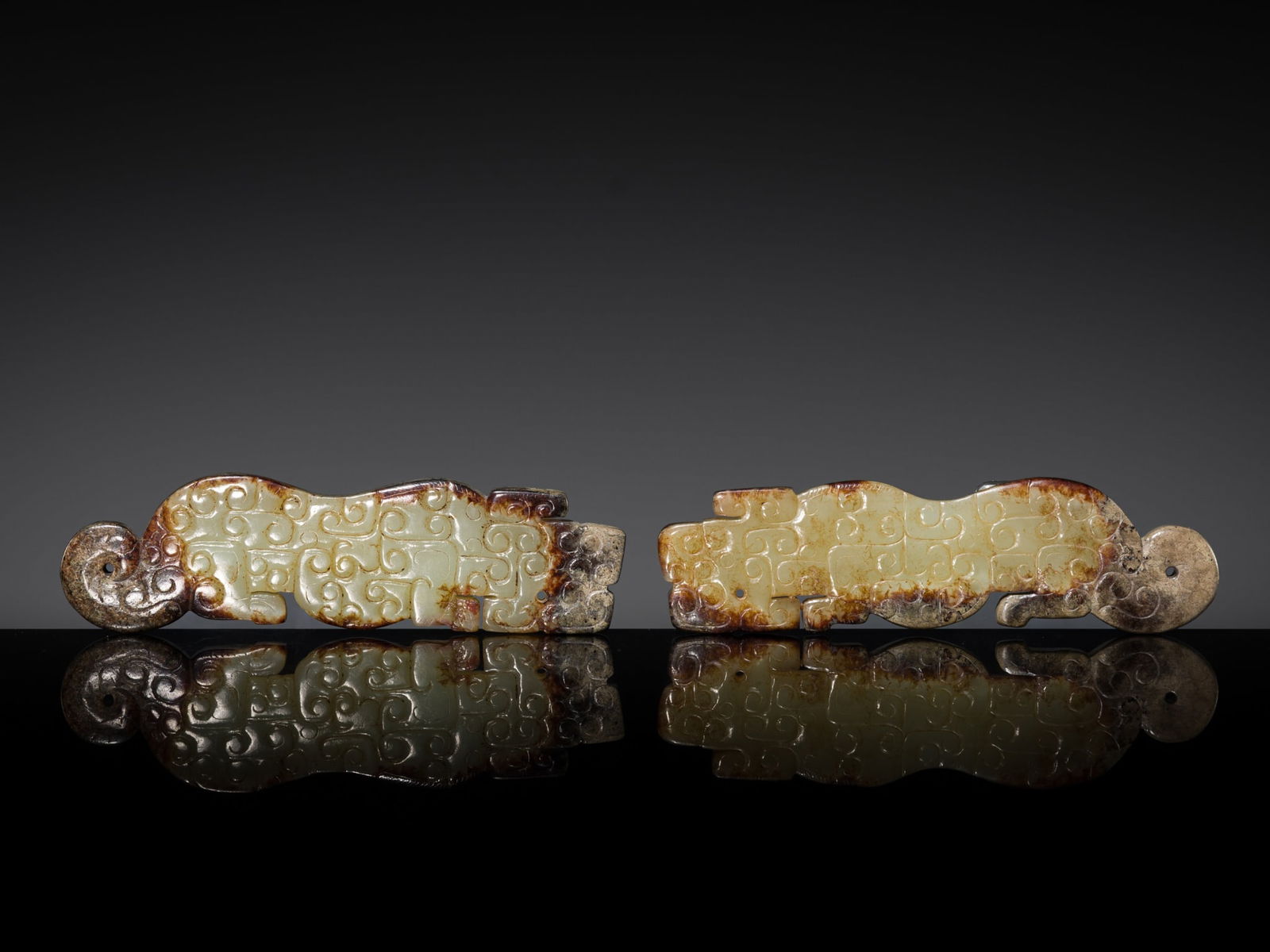 A PAIR OF CELADON AND RUSSET JADE 'TIGER' PENDANTS, EASTERN ZHOU TO WARRING STATES: A PAIR OF CELADON AND RUSSET JADE 'TIGER' PENDANTS, EASTERN ZHOU TO WARRING STATES China, 475-221 BC. Each of flattened form, elegantly carved to depict a crouching feline shown in profile and densel