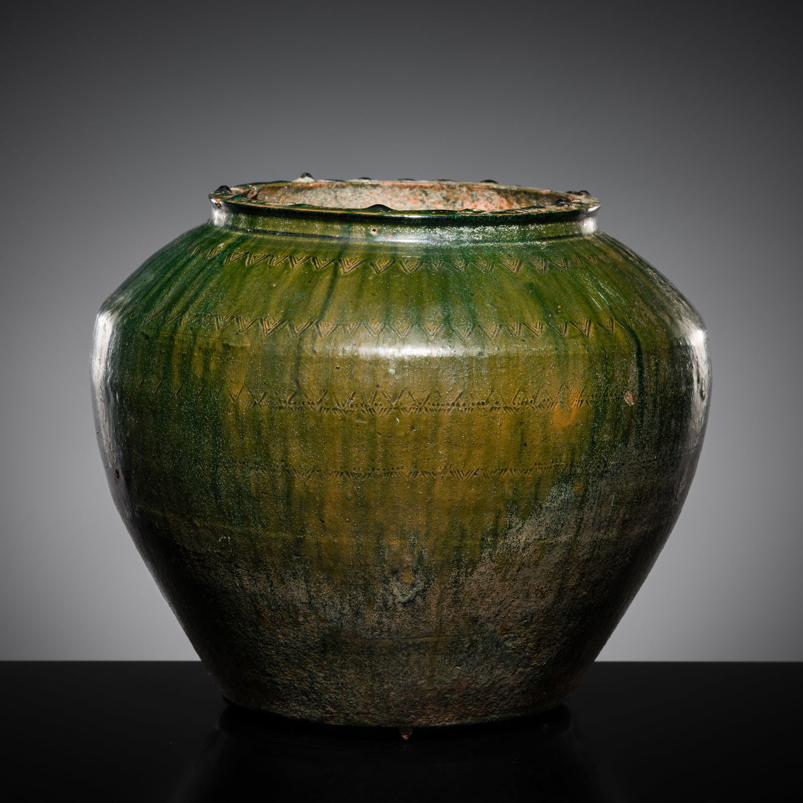 A CARVED GREEN GLAZED POTTERY JAR, HAN DYNASTY: A CARVED GREEN GLAZED POTTERY JAR, HAN DYNASTY This lot is from a single owner collection and is therefore offered without reserve China, 202 BC - 220 AD. Well potted with a high-shouldered body su