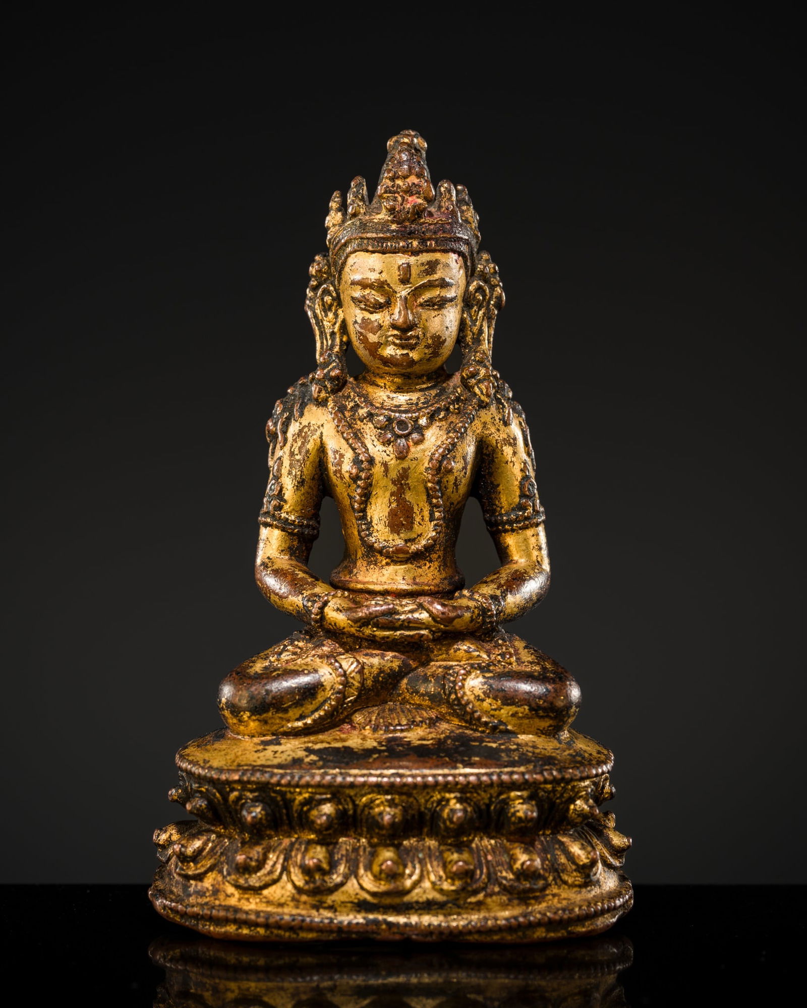 A SMALL GILT COPPER-ALLOY FIGURE OF AMITAYUS, NEPAL, 14TH-15TH CENTURY: A SMALL GILT COPPER-ALLOY FIGURE OF AMITAYUS, NEPAL, 14TH-15TH CENTURY Finely cast seated in dhyanasana on a double lotus base with beaded rims, the hands folded above the lap, dressed in a short dhot