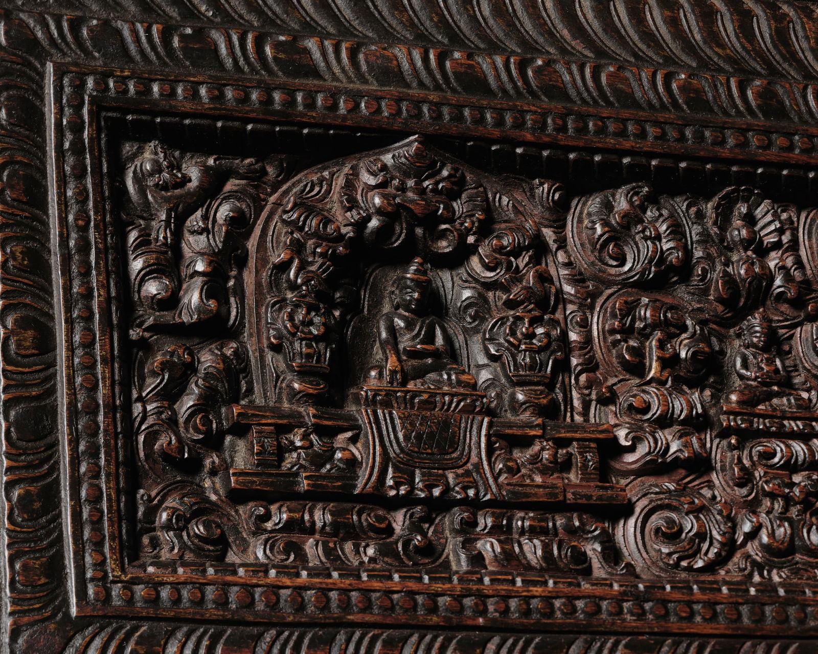 A RICHLY DETAILED WOOD MANUSCRIPT COVER, 14TH-15TH CENTURY: A RICHLY DETAILED WOOD MANUSCRIPT COVER, 14TH-15TH CENTURY Tibet. Finely and deeply carved, the three main deities each seated in dhyanasana on a lotus base atop a stepped throne supported by lions an