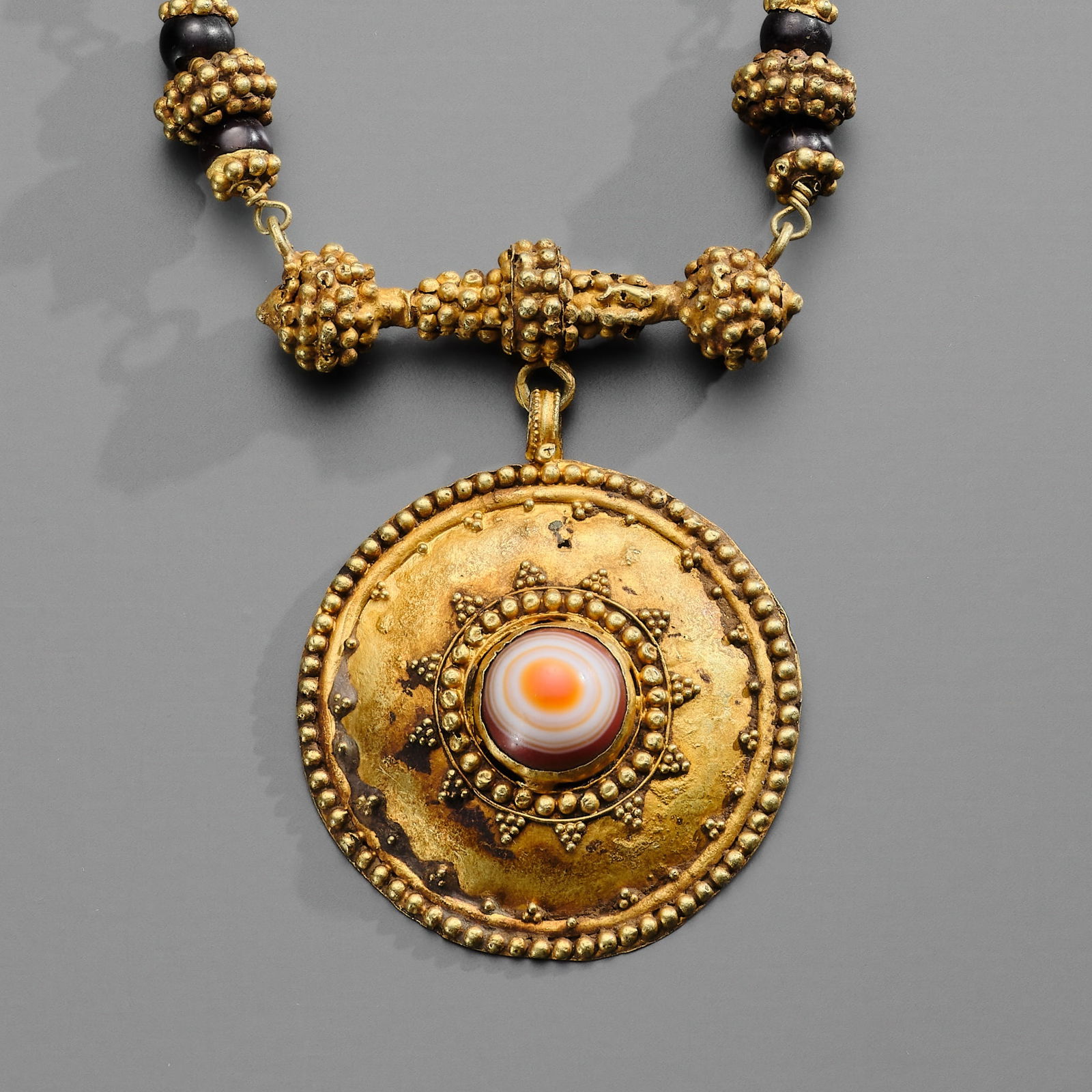 A GREEK GOLD, GARNET, AND SARDONYX NECKLACE, HELLENISTIC PERIOD, CIRCA 2ND-1ST CENTURY BC: A GREEK GOLD, GARNET, AND SARDONYX NECKLACE, HELLENISTIC PERIOD, CIRCA 2ND-1ST CENTURY BC Centered by a large circular medallion with a box-set oval sardonyx fringed with granulation, suspended on a w