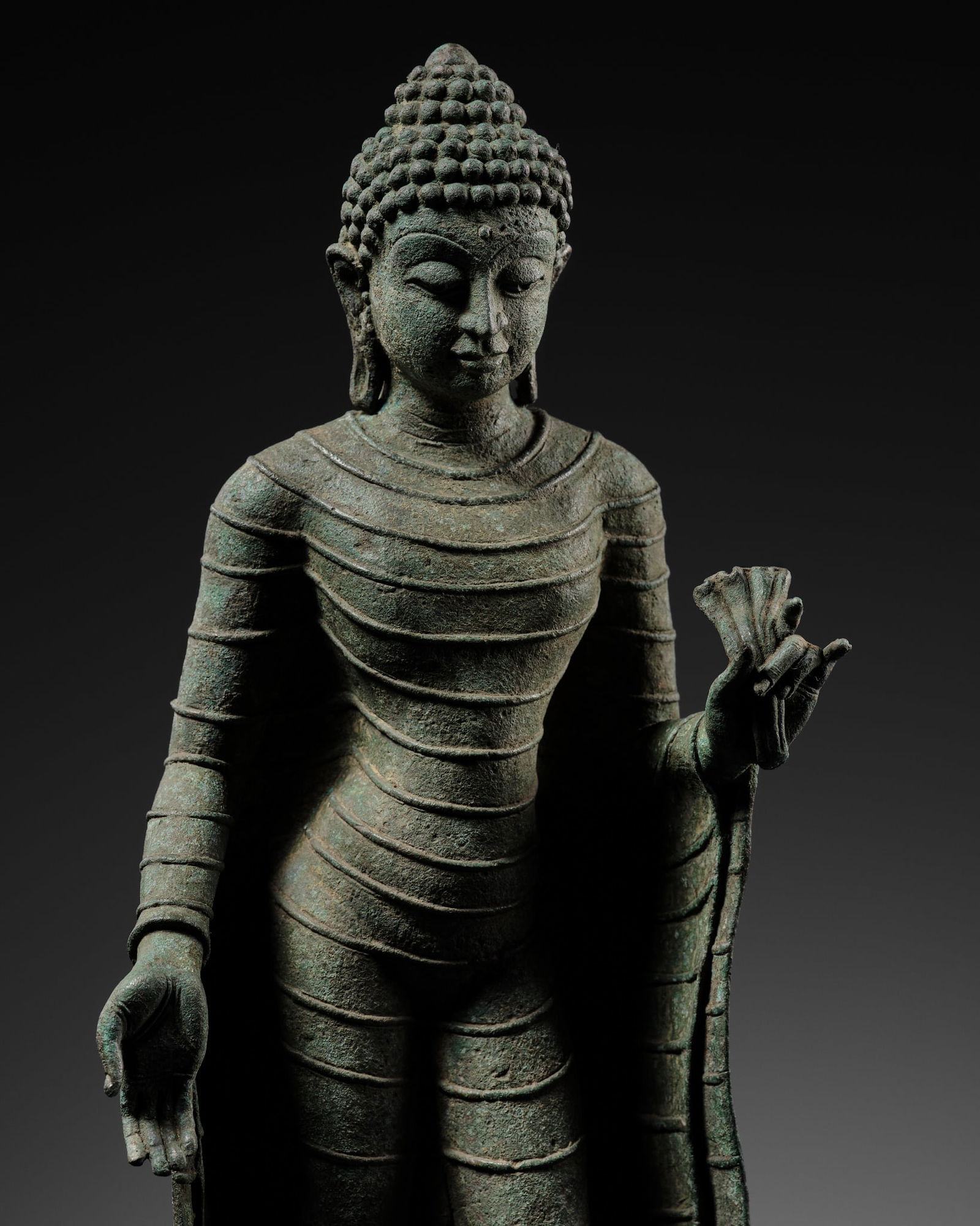 A BRONZE FIGURE OF THE STANDING BUDDHA, SRIVIJAYA, WESTERN INDONESIA, 8TH-10TH CENTURY: A BRONZE FIGURE OF THE STANDING BUDDHA, SRIVIJAYA, WESTERN INDONESIA, 8TH-10TH CENTURY Finely cast standing in a slight tribhanga, the right hand lowered in varada mudra, the left raised and held in k