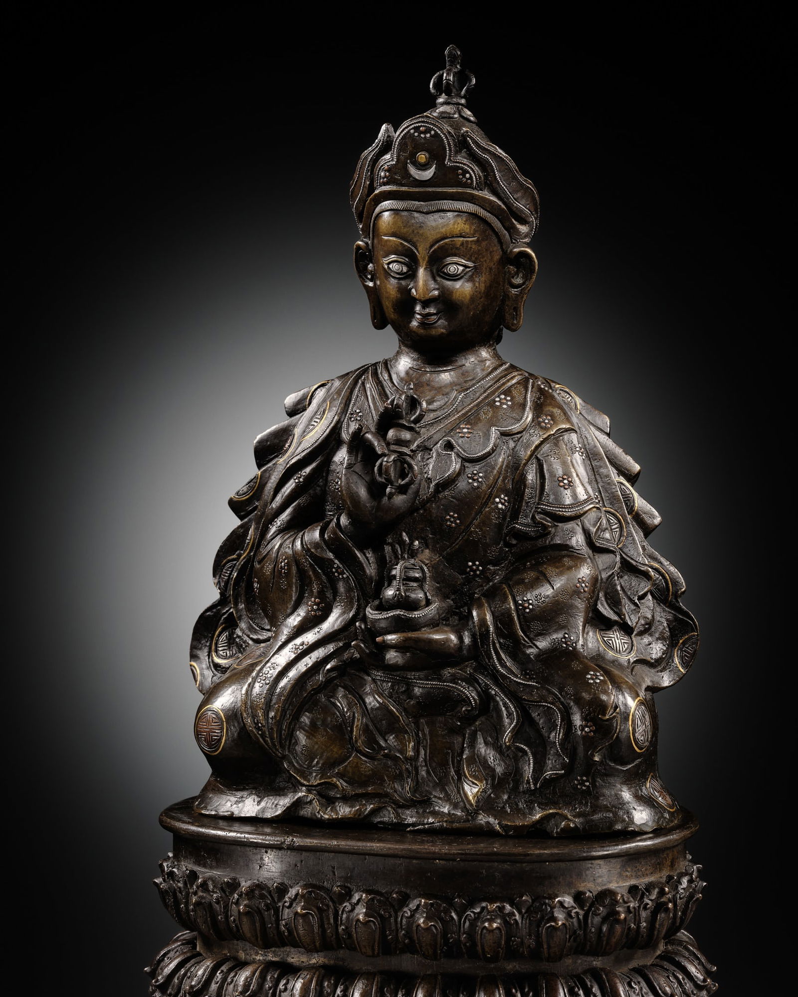 A LARGE GOLD, SILVER, AND COPPER INLAID BRONZE FIGURE OF PADMASAMBHAVA, 17TH-18TH CENTURY: A LARGE GOLD, SILVER, AND COPPER INLAID BRONZE FIGURE OF PADMASAMBHAVA, 17TH-18TH CENTURY Central Himalayan regions, probably Tibet or Bhutan. Seated in dhyanasana atop a separately cast double-lotus