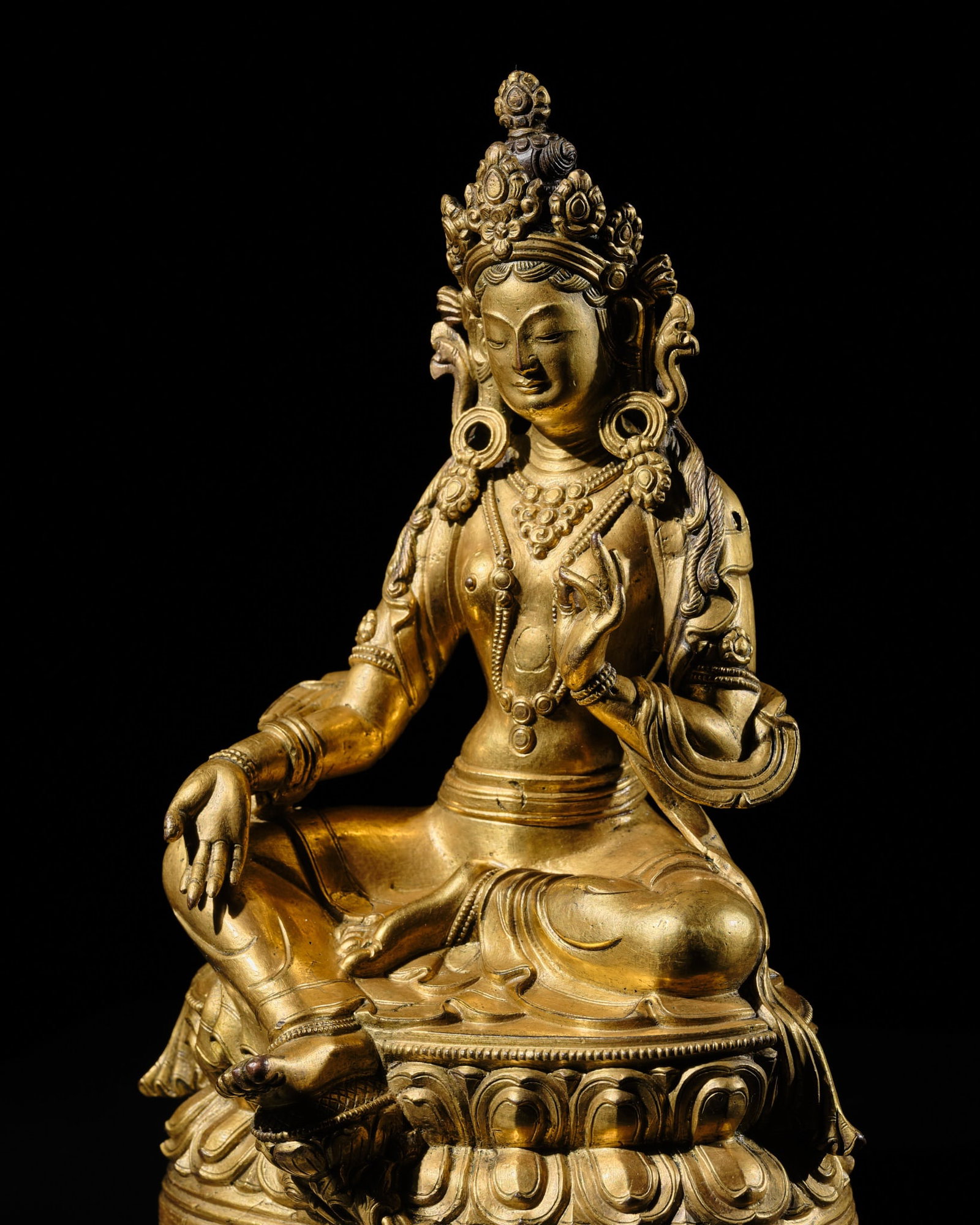 A GILT-BRONZE FIGURE OF GREEN TARA, TIBETAN-CHINESE, 18TH CENTURY: A GILT-BRONZE FIGURE OF GREEN TARA, TIBETAN-CHINESE, 18TH CENTURY Elegantly cast, seated in lalitasana on a double-lotus base with a beaded edge, her pendent right leg supported by a separate lotus bl