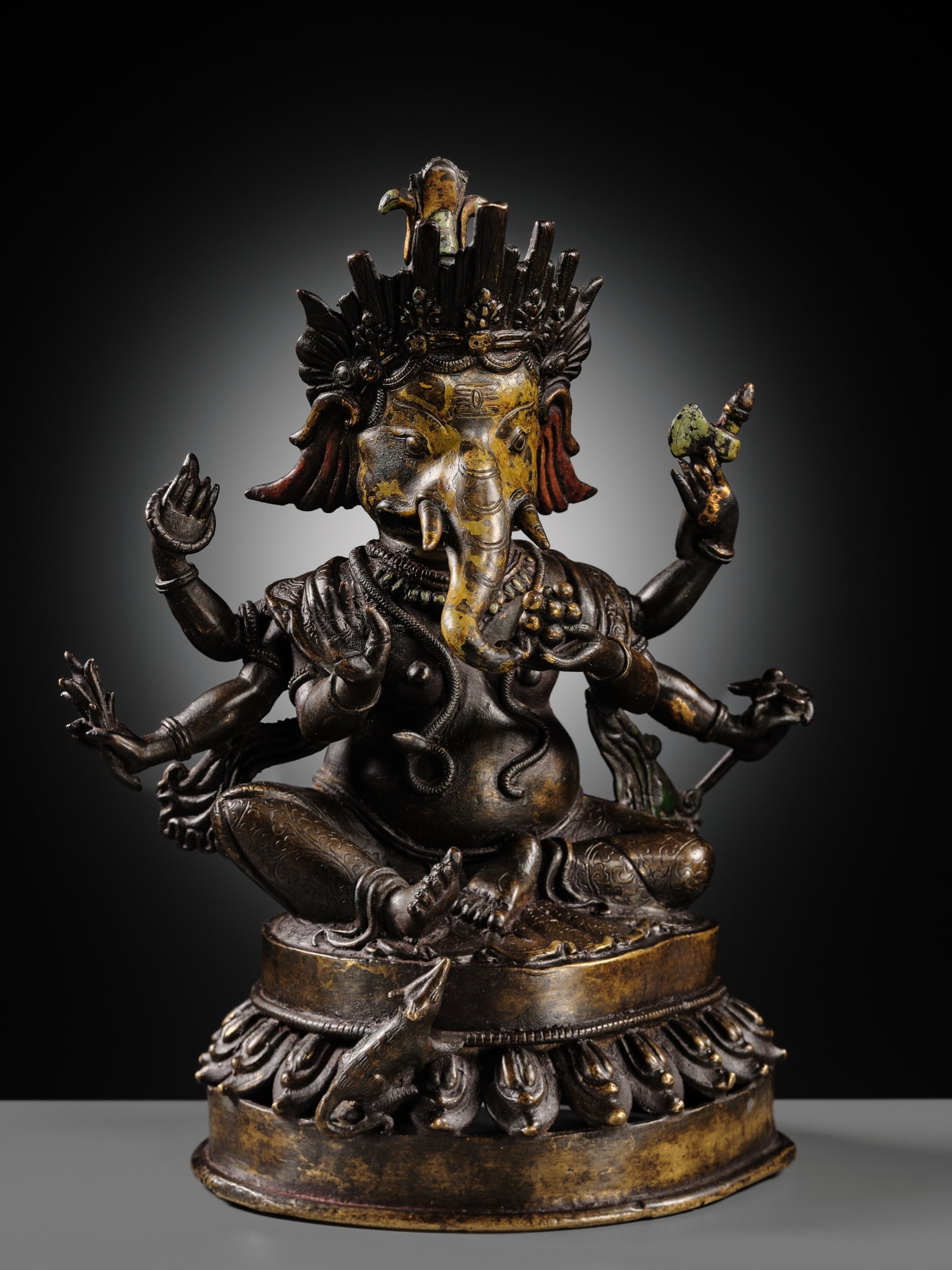 A LACQUERED COPPER ALLOY FIGURE OF GANESHA, 18TH-19TH CENTURY: A LACQUERED COPPER ALLOY FIGURE OF GANESHA, 18TH-19TH CENTURY Nepal, Kathmandu Valley. The six-armed deity seated atop a pierced lotus base, dressed in a finely incised dhoti, a snake writhing around