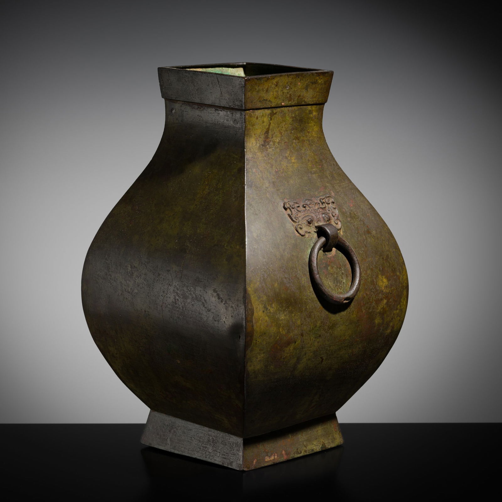 AN ARCHAIC BRONZE STORAGE VESSEL, FANGHU, HAN DYNASTY: AN ARCHAIC BRONZE STORAGE VESSEL, FANGHU, HAN DYNASTY China, 206 BC-220 AD. The tall, square vessel raised on a spreading foot, with plain curved sides narrowing to the neck set off by a lozenge-shape