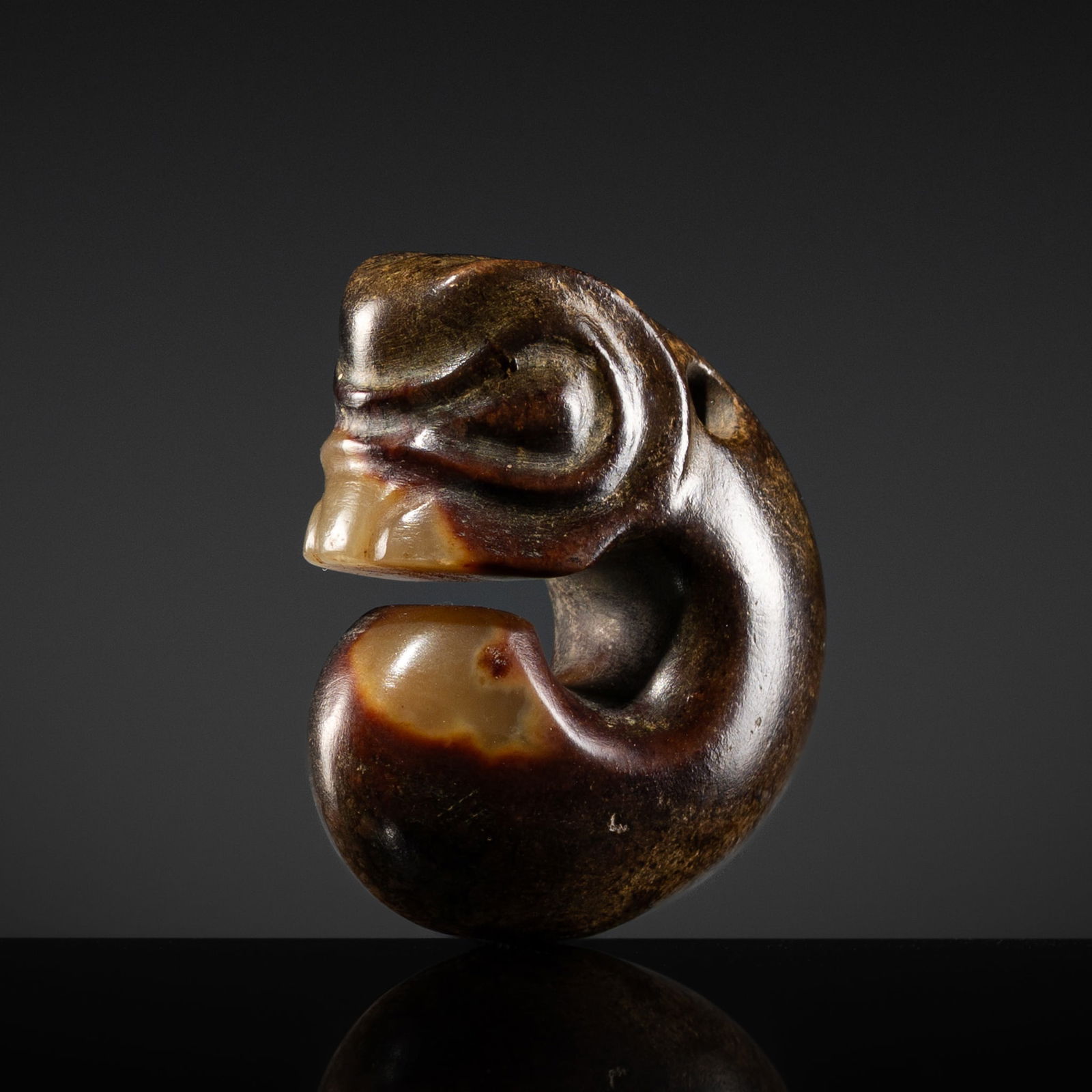 A RUSSET-BROWN AND YELLOW JADE 'PIG-DRAGON' PENDANT, ZHULONG, HONGSHAN CULTURE: A RUSSET-BROWN AND YELLOW JADE 'PIG-DRAGON' PENDANT, ZHULONG, HONGSHAN CULTURE China, Neolithic period, 4700-2500 BC. Of iconic form, the coiled body and superbly rendered head subtly detailed with bu