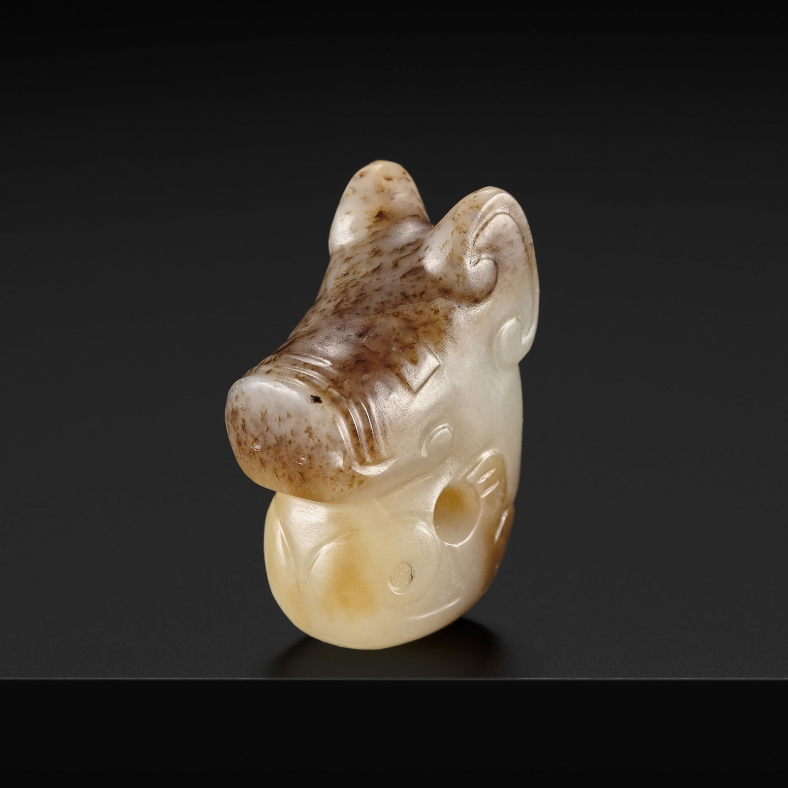 A BROWN AND WHITE JADE 'PIG DRAGON' PENDANT, ZHULONG, LATE SHANG DYNASTY: A BROWN AND WHITE JADE 'PIG DRAGON' PENDANT, ZHULONG, LATE SHANG DYNASTY China, Henan province, Anyang. Finely carved as the coiled mythical animal, pierced at the center, the face reminiscent of a pi