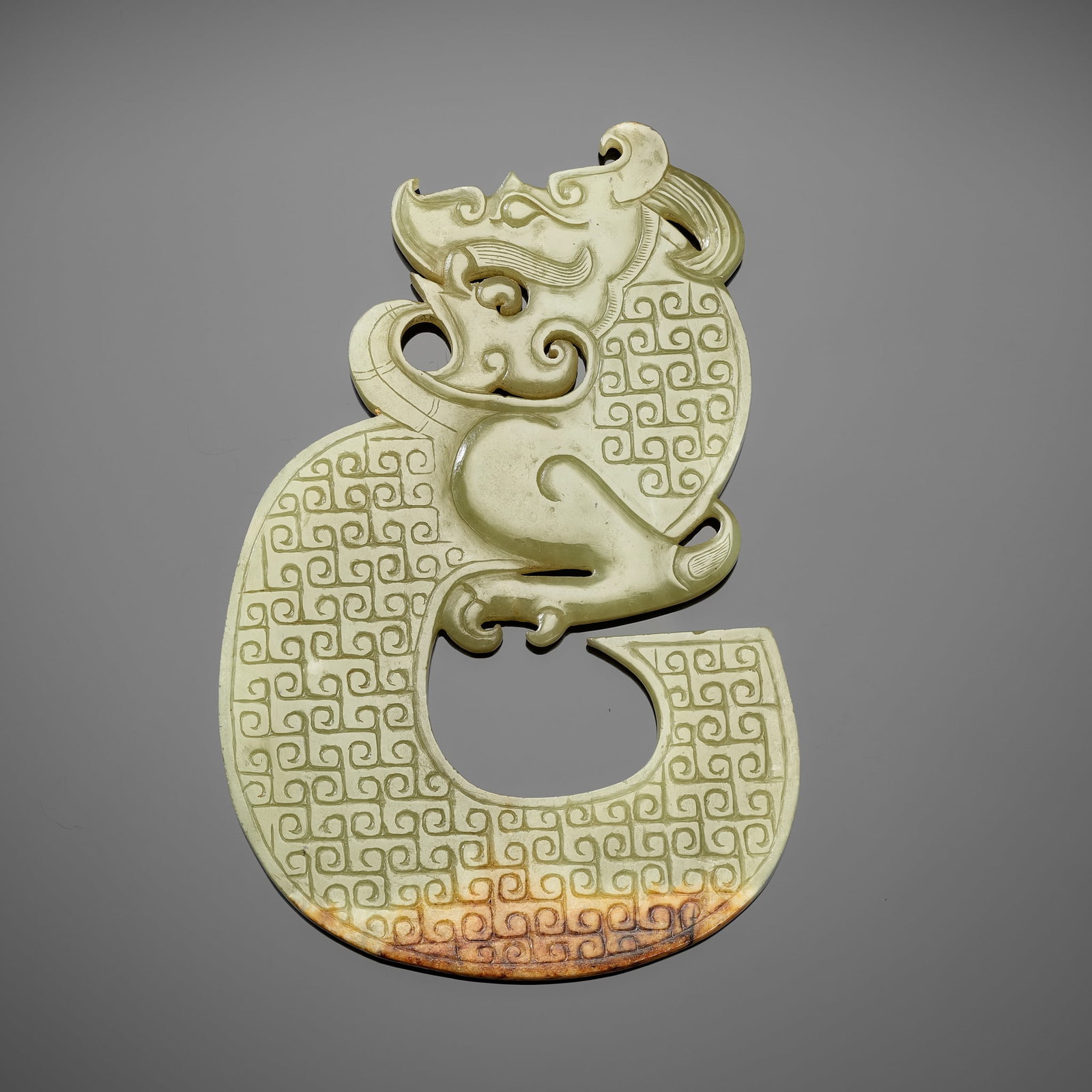 A GREEN AND RUSSET 'DRAGON' PENDANT, HAN DYNASTY: A GREEN AND RUSSET 'DRAGON' PENDANT, HAN DYNASTY China, 206 BC-220 AD. Of flattened S-shape, incised to both sides, the face with bulging eyes above a moustache, surmounted by prominent horns, the bod