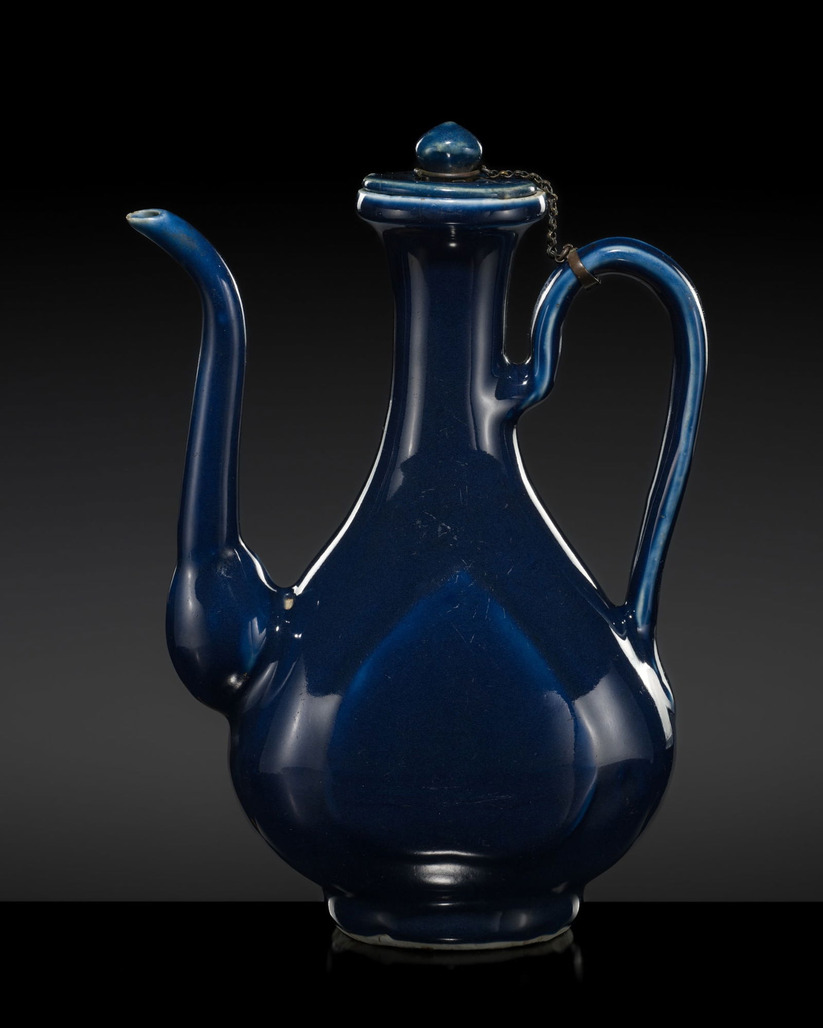 A BLUE-GLAZED EWER AND COVER, MING DYNASTY: A BLUE-GLAZED EWER AND COVER, MING DYNASTY China, 16th century. Finely potted with a pear-shaped body supported on a short foot and rising to a long slender neck with a dish-shaped mouth, surmounted b
