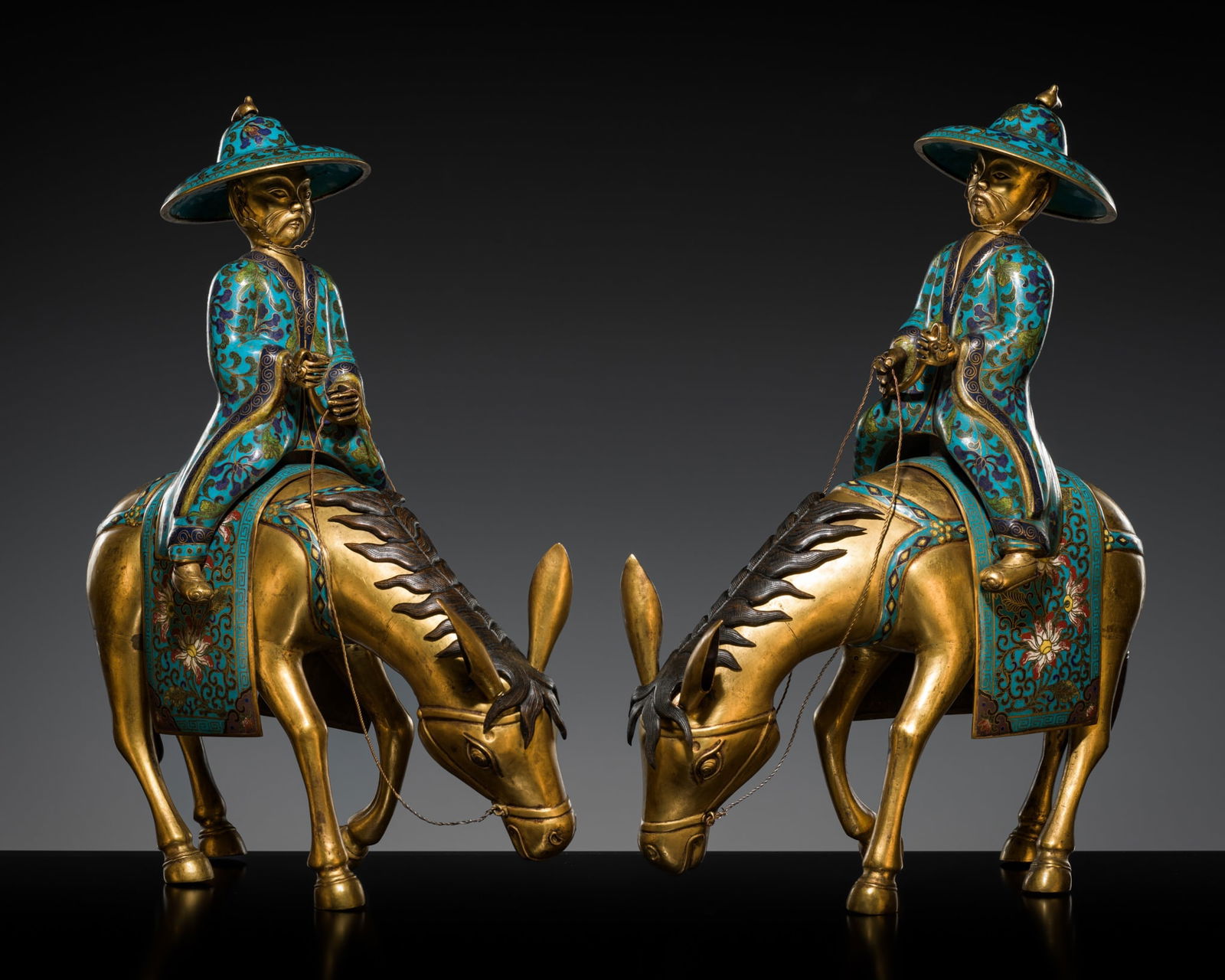 A PAIR OF GILT-BRONZE CLOISONNE ENAMEL RIDERS ON MULES, QING DYNASTY: A PAIR OF GILT-BRONZE CLOISONNE ENAMEL RIDERS ON MULES, QING DYNASTY China, 19th century. Finely cast in mirror image, depicting two bearded men wearing long cloaks and wide-brimmed hats decorated wit