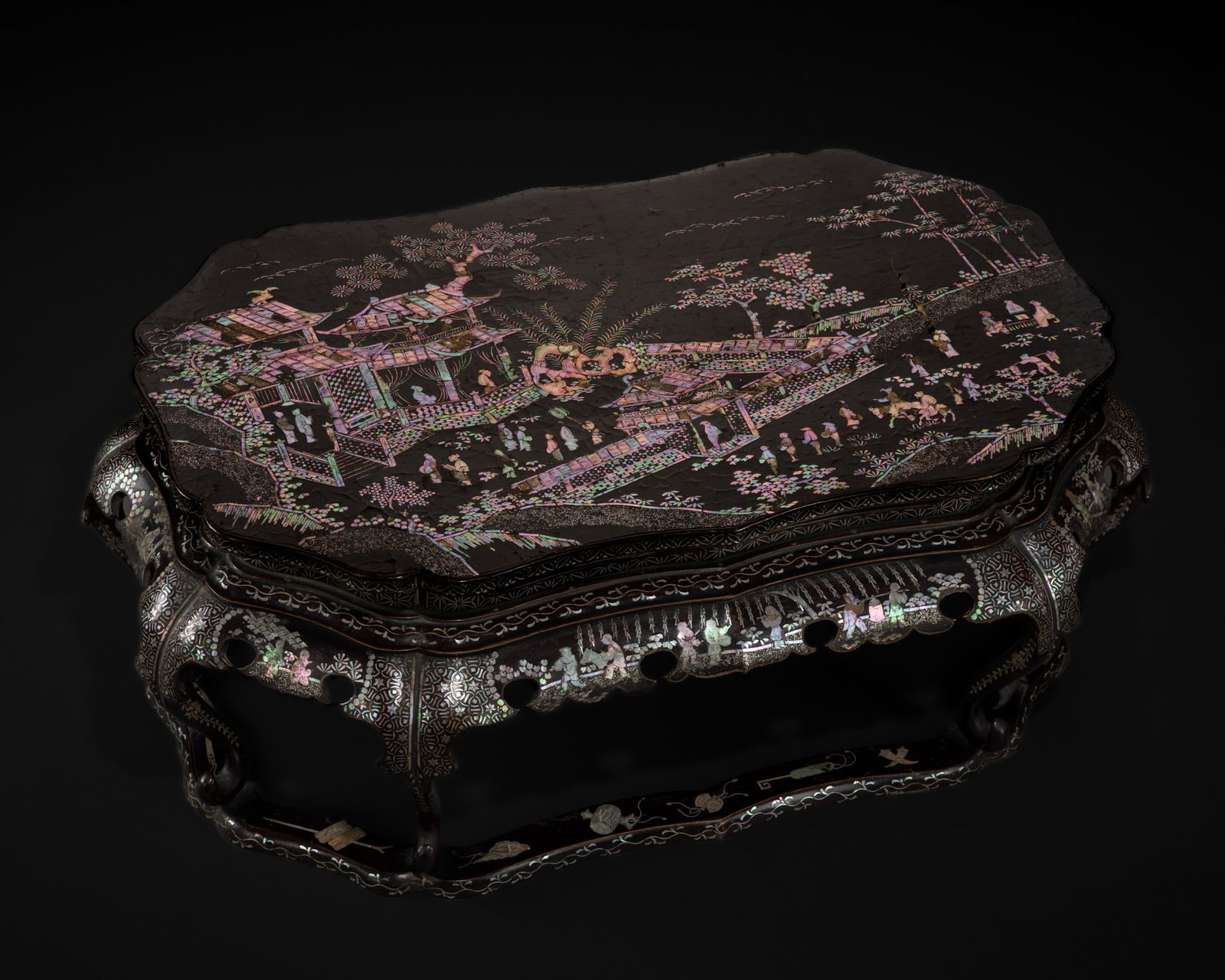 A MOTHER-OF-PEARL-INLAID BLACK LACQUER LOW TABLE, KANGXI PERIOD: A MOTHER-OF-PEARL-INLAID BLACK LACQUER LOW TABLE, KANGXI PERIOD China. The hexafoil tabletop is finely inlaid in mother-of-pearl with figures gathered within a pavilion complex along a riverbank, fram