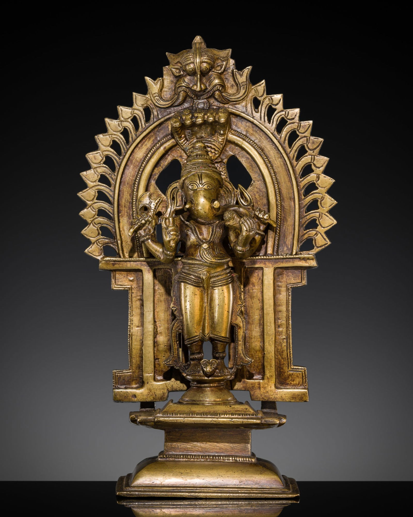 A BRASS SHRINE WITH A FIGURE OF GANESHA, SOUTH INDIA, 19TH CENTURY: A BRASS SHRINE WITH A FIGURE OF GANESHA, SOUTH INDIA, 19TH CENTURY Separately cast in three parts, the deity standing in samabhanga atop a waisted pedestal with his rat vahana crouching between his fe