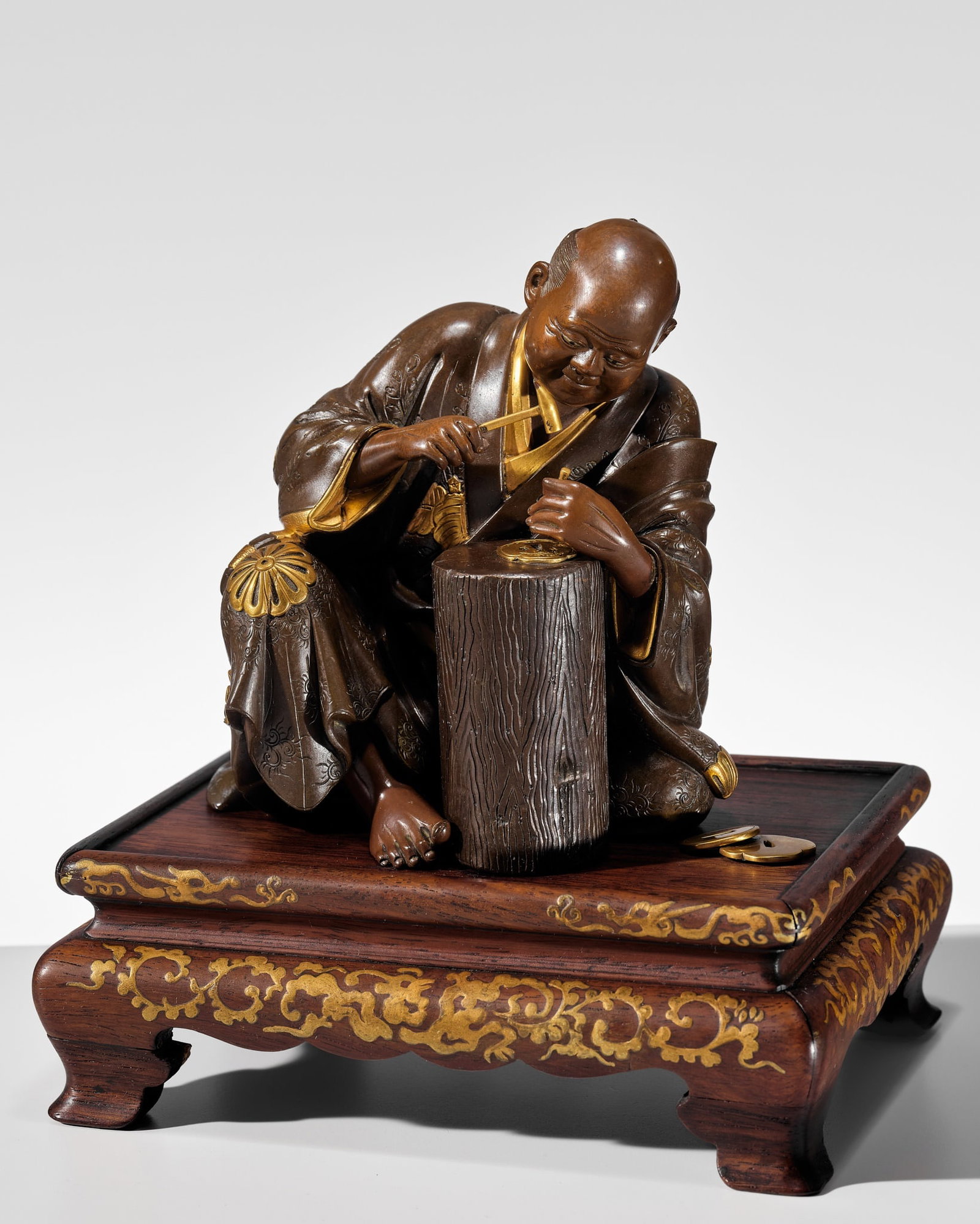 MIYAO: A FINE PARCEL-GILT BRONZE OKIMONO OF A TSUBA MAKER: MIYAO: A FINE PARCEL-GILT BRONZE OKIMONO OF A TSUBA MAKER By the Miyao company of Yokohama, signed Miyao ko Japan, Meiji period (1868-1912) Finely cast, the elderly master is depicted seated beside a 