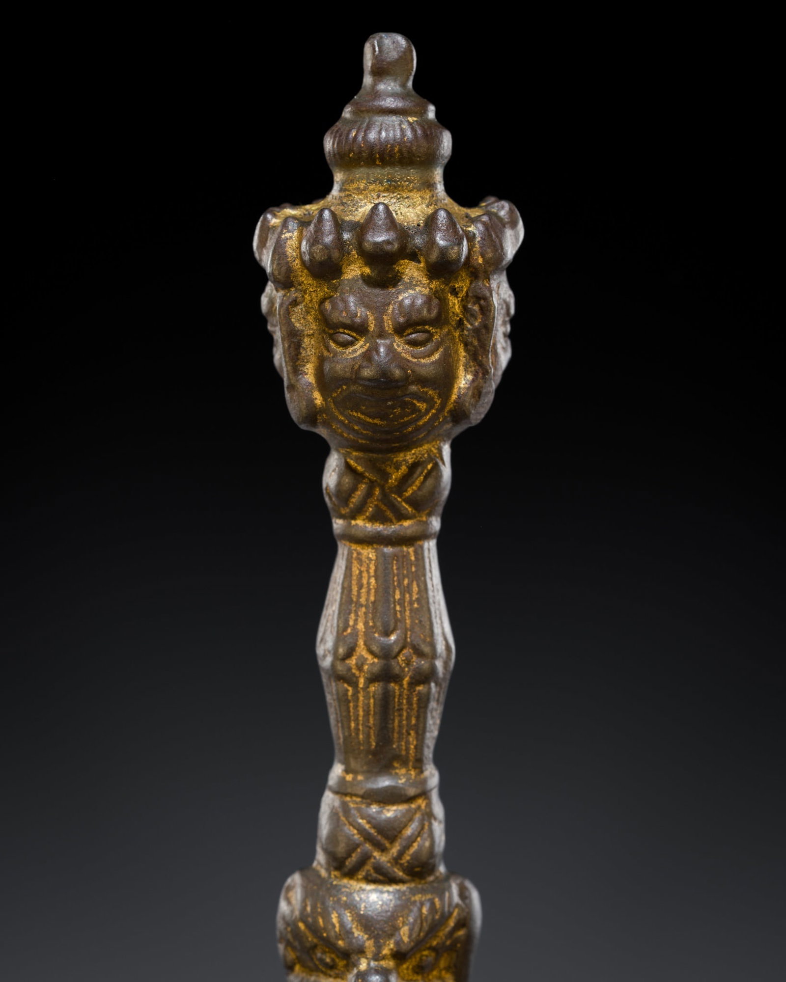 A GILT-IRON VAJRAKILA PHURBA, TIBET, 19TH CENTURY: A GILT-IRON VAJRAKILA PHURBA, TIBET, 19TH CENTURY The pommel cast as a three-headed wrathful deity with wide bulging eyes below furrowed brows centered by a protruding third eye, and grim tight-lipped