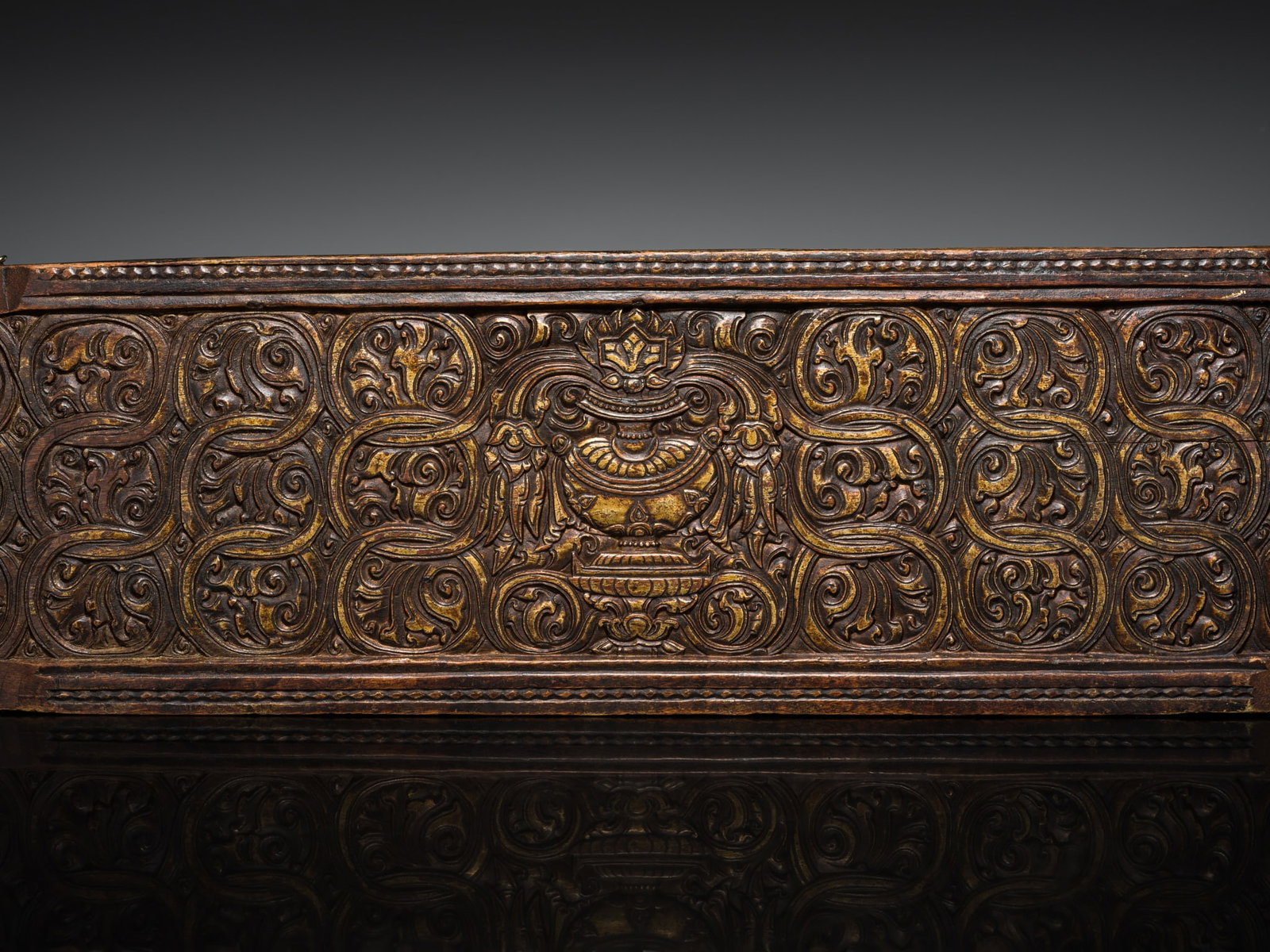 A FINE GILT WOOD MANUSCRIPT COVER, 15TH CENTURY: A FINE GILT WOOD MANUSCRIPT COVER, 15TH CENTURY Tibet. Finely carved in relief with an amrita vessel at the center, surrounded by three rows of scrolling vines to each side, all within a beaded border