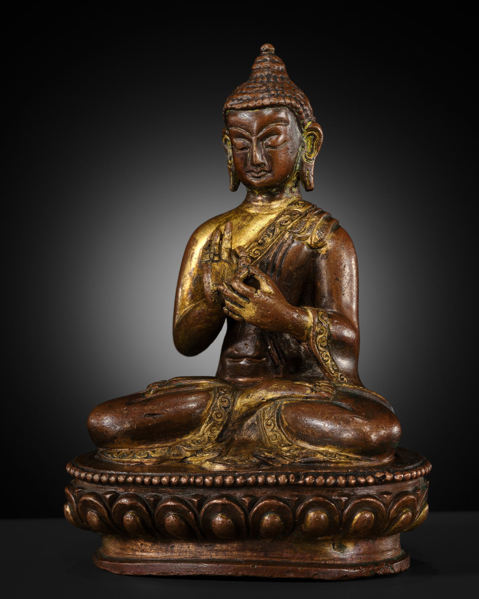 A SMALL PARCEL-GILT COPPER ALLOY FIGURE OF BUDDHA, TIBET OR NEPAL, 17TH-18TH CENTURY: A SMALL PARCEL-GILT COPPER ALLOY FIGURE OF BUDDHA, TIBET OR NEPAL, 17TH-18TH CENTURY Finely cast seated in dhyanasana above a lotus base with a beaded upper rim, the hands held before the chest in dha
