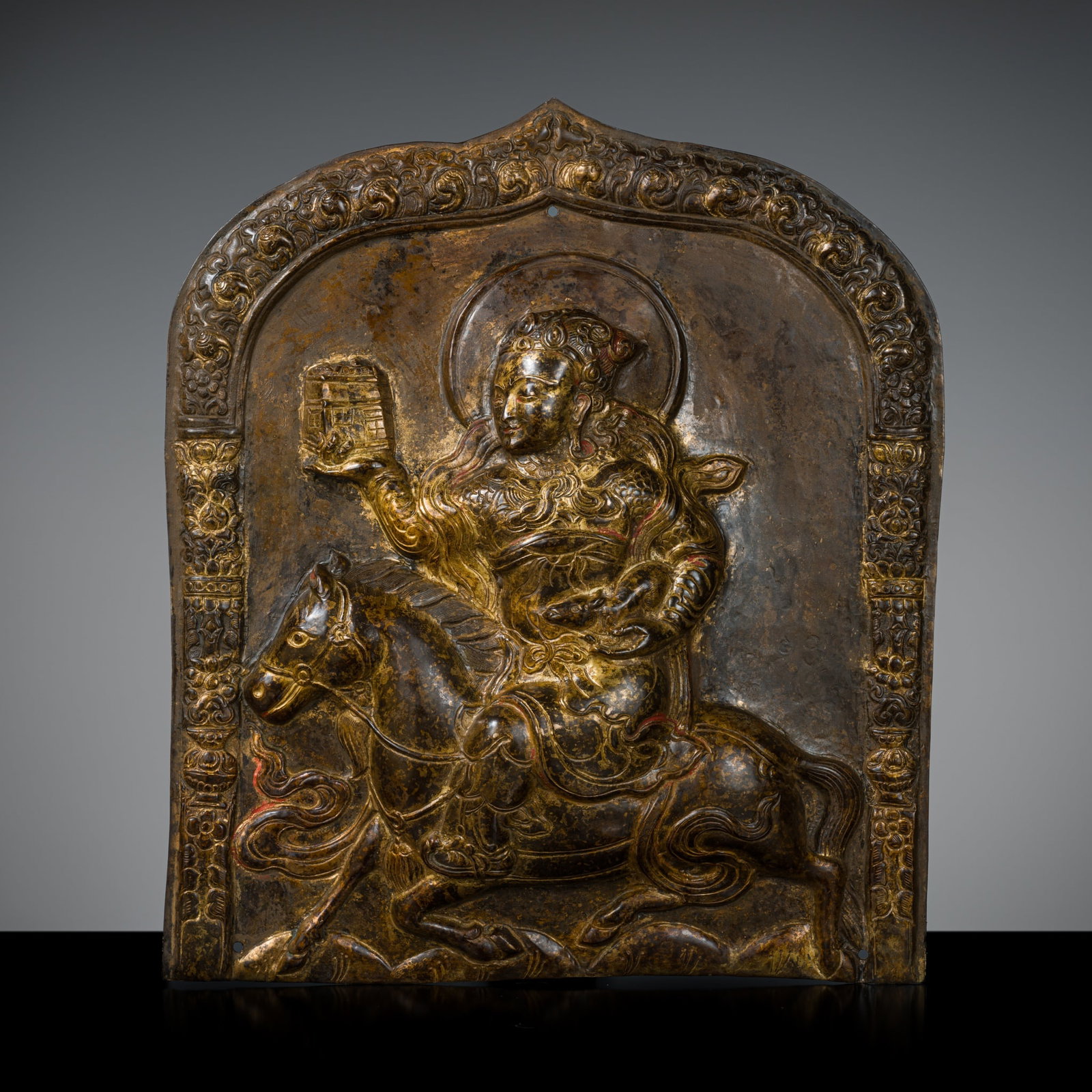 A GILT COPPER-ALLOY REPOUSSÉ PLAQUE OF PANCHIKA, TIBET, 17TH-18TH CENTURY: A GILT COPPER-ALLOY REPOUSSÉ PLAQUE OF PANCHIKA, TIBET, 17TH-18TH CENTURY Tibet, 17th century. Panchika, one of the eight horsemen of Vaishravana, identified by the palace held in his right hand,