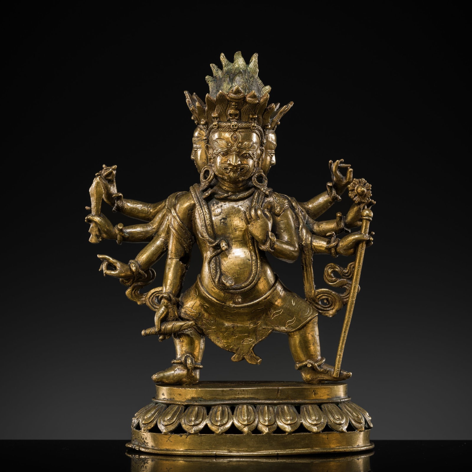 A GILT-BRONZE FIGURE OF MAHAKALA, TIBET, 18TH CENTURY: A GILT-BRONZE FIGURE OF MAHAKALA, TIBET, 18TH CENTURY Cast in two parts, the eight-armed wrathful deity standing in dynamic pose atop a pierced lotus base, holding attributes including vajra, sword, s