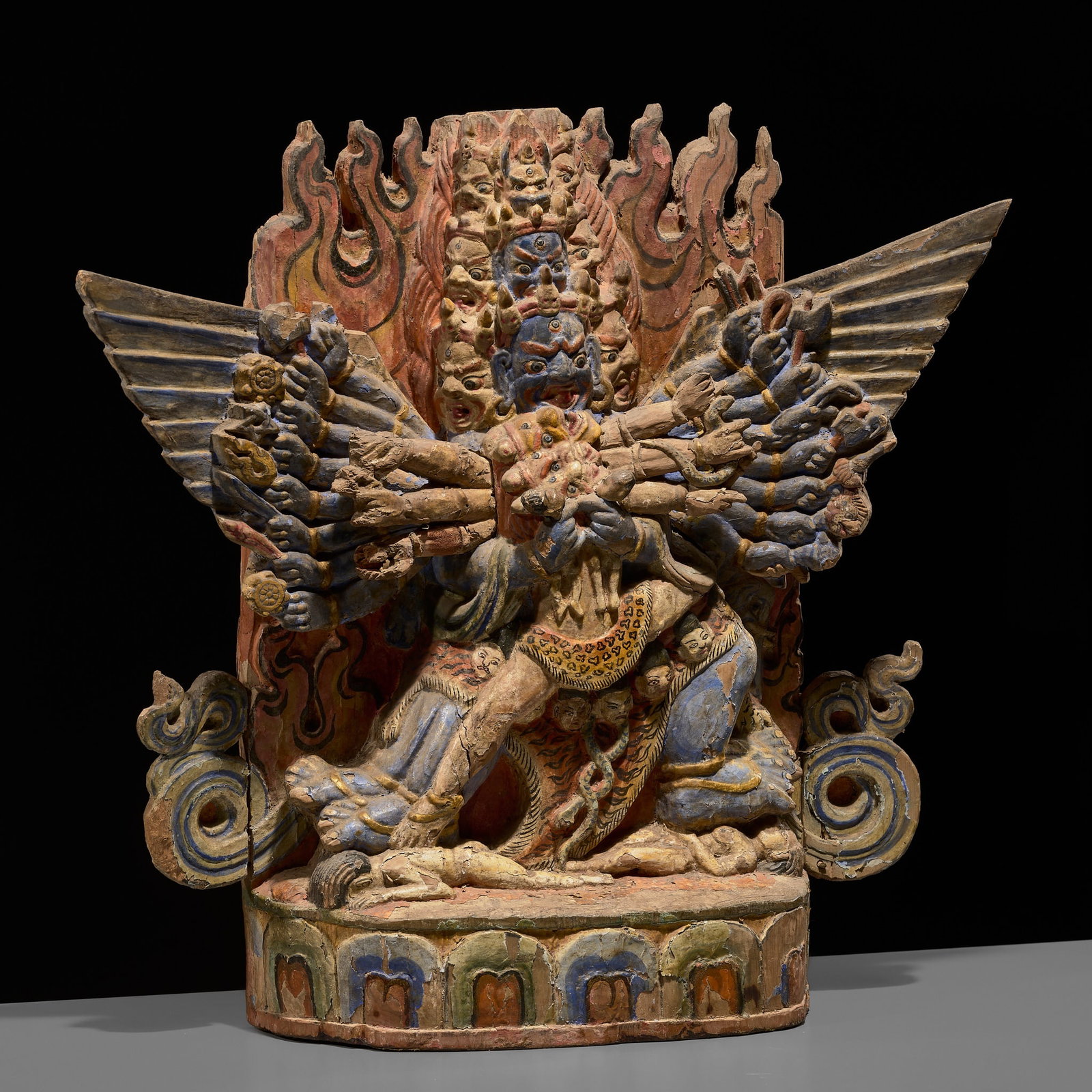 A POLYCHROME WOOD FIGURE OF WALCHEN GEKHO, TIBET, 18TH CENTURY: A POLYCHROME WOOD FIGURE OF WALCHEN GEKHO, TIBET, 18TH CENTURY Finely carved, the fierce blue god is vibrantly depicted here with nine faces, eighteen hands and four legs. Each of his wrathful faces h