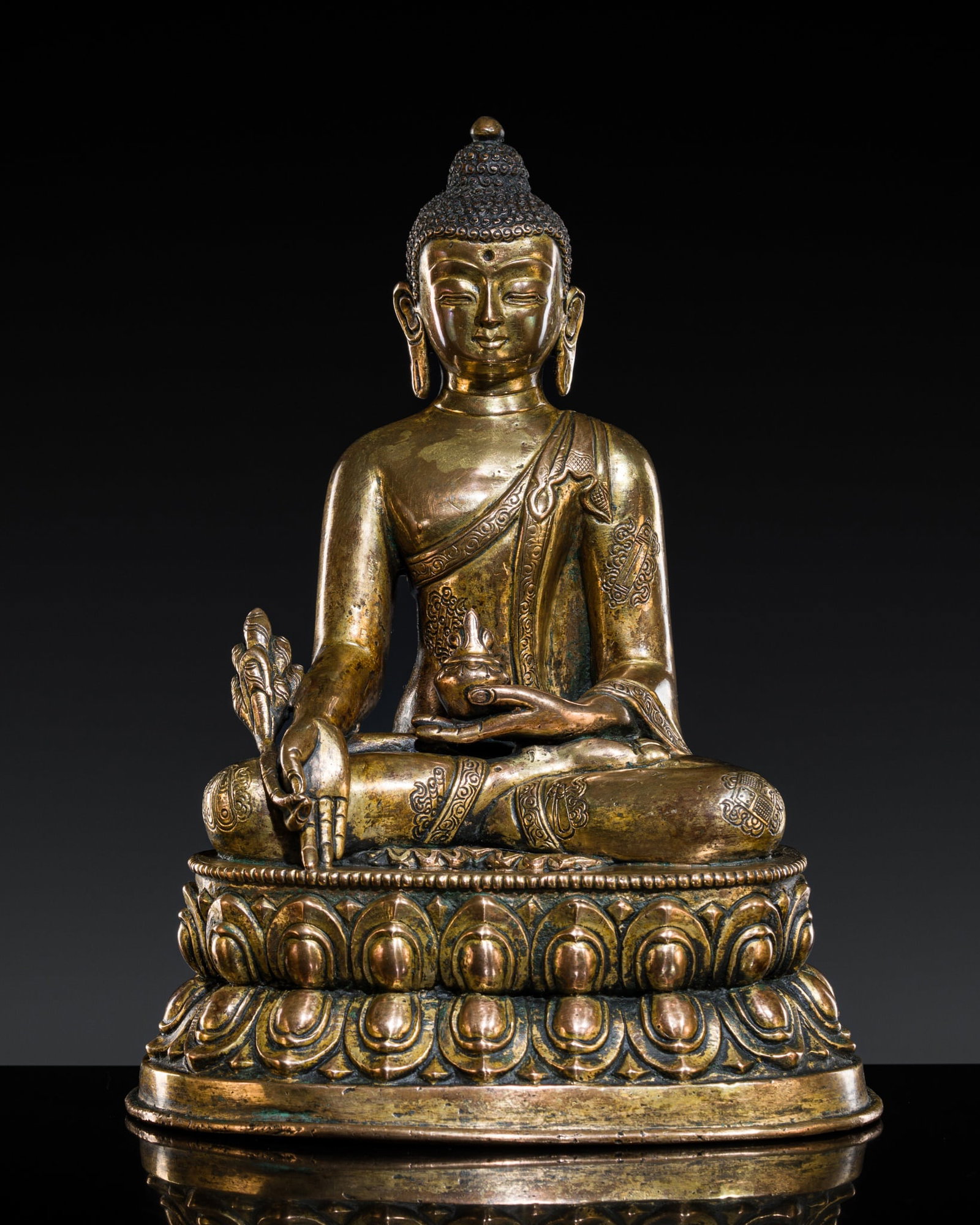 A GILT COPPER-ALLOY FIGURE OF THE MEDICINE BUDDHA, BHAISHAJYAGURU, TIBET, 19TH CENTURY: A GILT COPPER-ALLOY FIGURE OF THE MEDICINE BUDDHA, BHAISHAJYAGURU, TIBET, 19TH CENTURY Finely cast seated in dhyanasana on a double-lotus base with beaded edges, his left hand lowered in dhyana mudra,