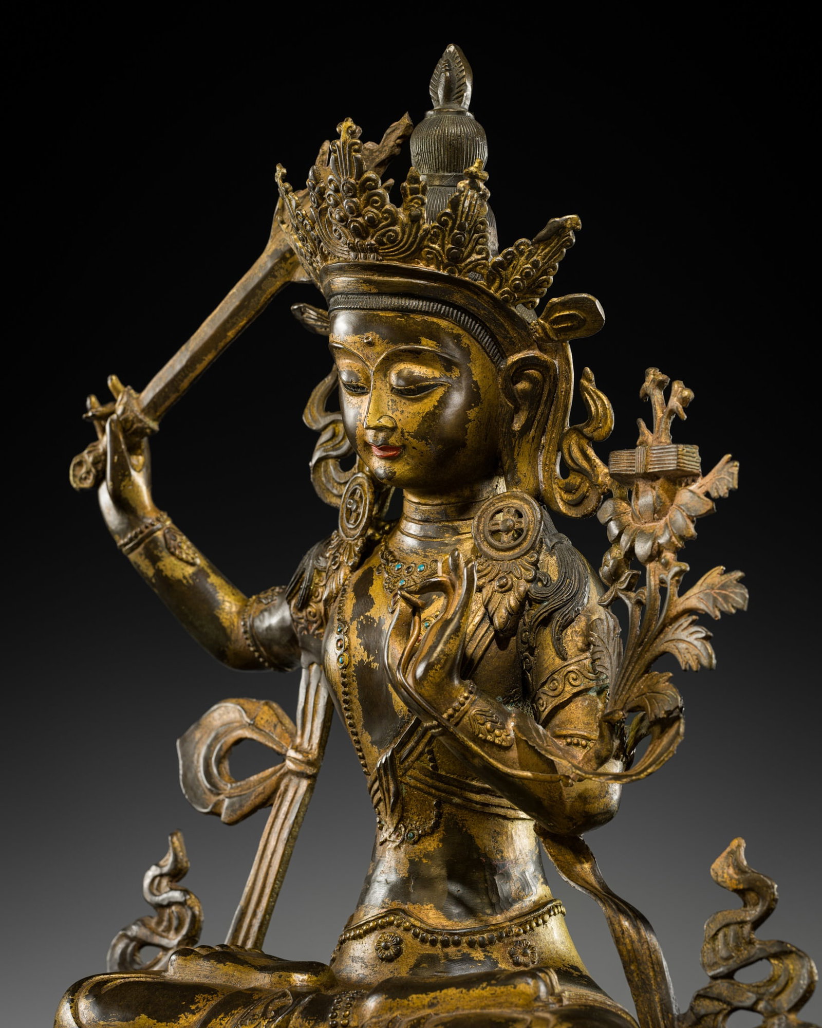 A LARGE (66 CM) INLAID GILT-COPPER ALLOY FIGURE OF MANJUSHRI, NEPAL, EARLY TO MID-20TH CENTURY: A LARGE (66 CM) INLAID GILT-COPPER ALLOY FIGURE OF MANJUSHRI, NEPAL, EARLY TO MID-20TH CENTURY Finely cast seated in dhyanasana atop a waisted lotus base with a beaded rim, holding aloft a separately 