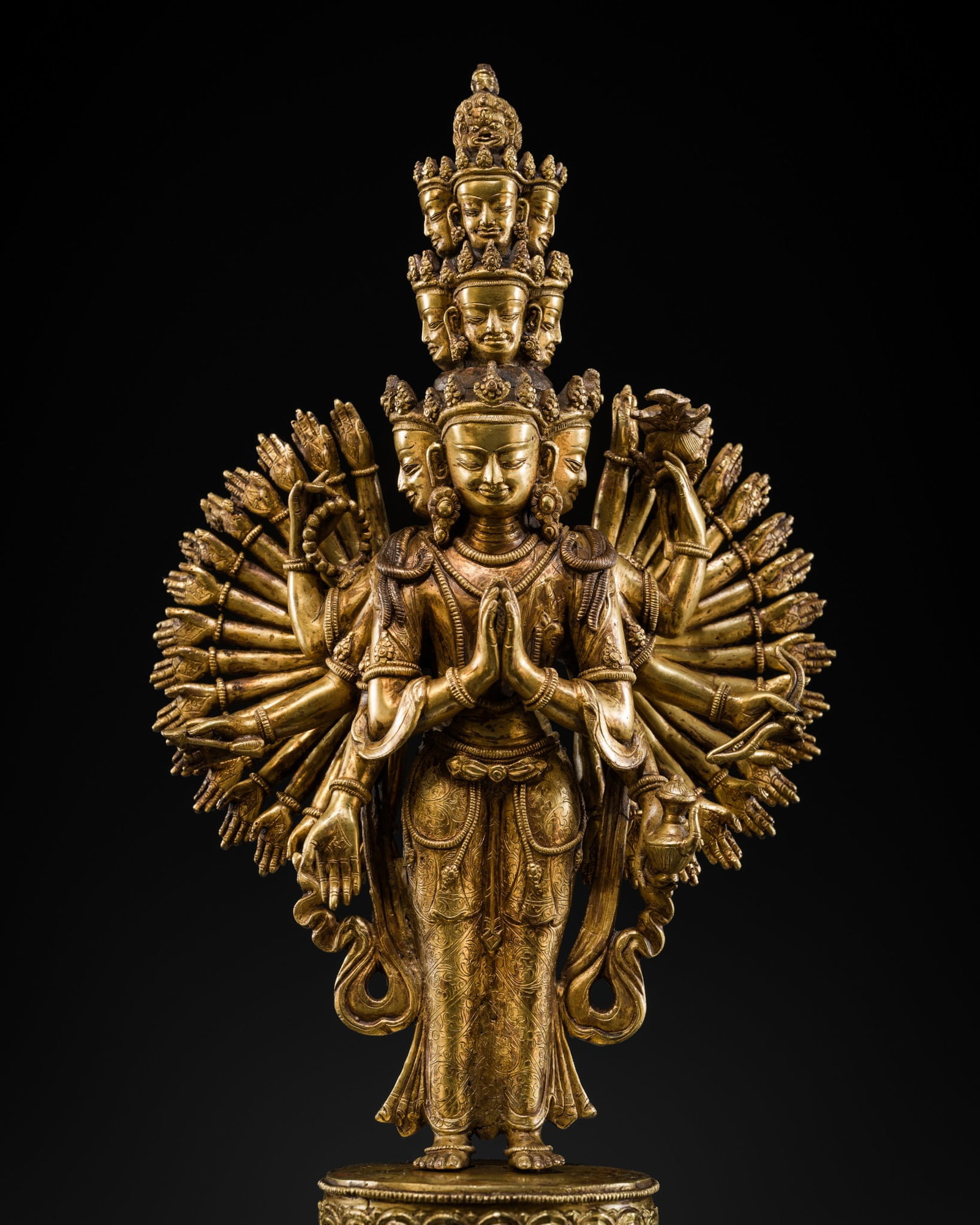A GILT COPPER ALLOY FIGURE OF AVALOKITESHVARA SAHASHRABHUJA EKADASHAMUKHA, TIBETAN-CHINESE, EARLY: A GILT COPPER ALLOY FIGURE OF AVALOKITESHVARA SAHASHRABHUJA EKADASHAMUKHA, TIBETAN-CHINESE, EARLY 20TH CENTURY Heavily and separately cast, Avalokiteshvara stands in samabhanga on a beaded double-lotu
