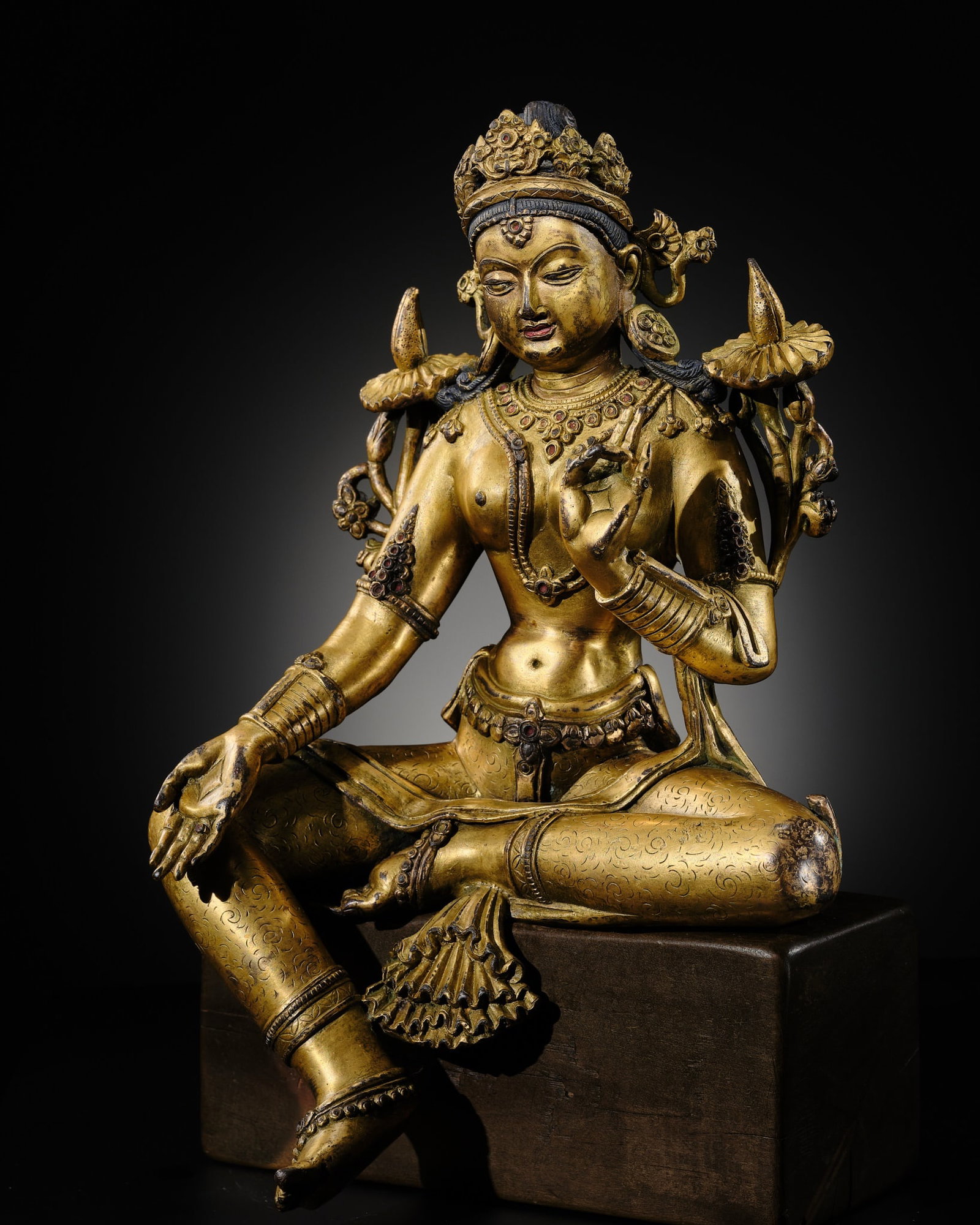 A GILT-BRONZE FIGURE OF GREEN TARA, NEPAL: A GILT-BRONZE FIGURE OF GREEN TARA, NEPAL Finely modeled, the deity seated in lalitasana, her right hand held in varada mudra and the left raised in vitarka mudra, each holding the stem of a flower wh