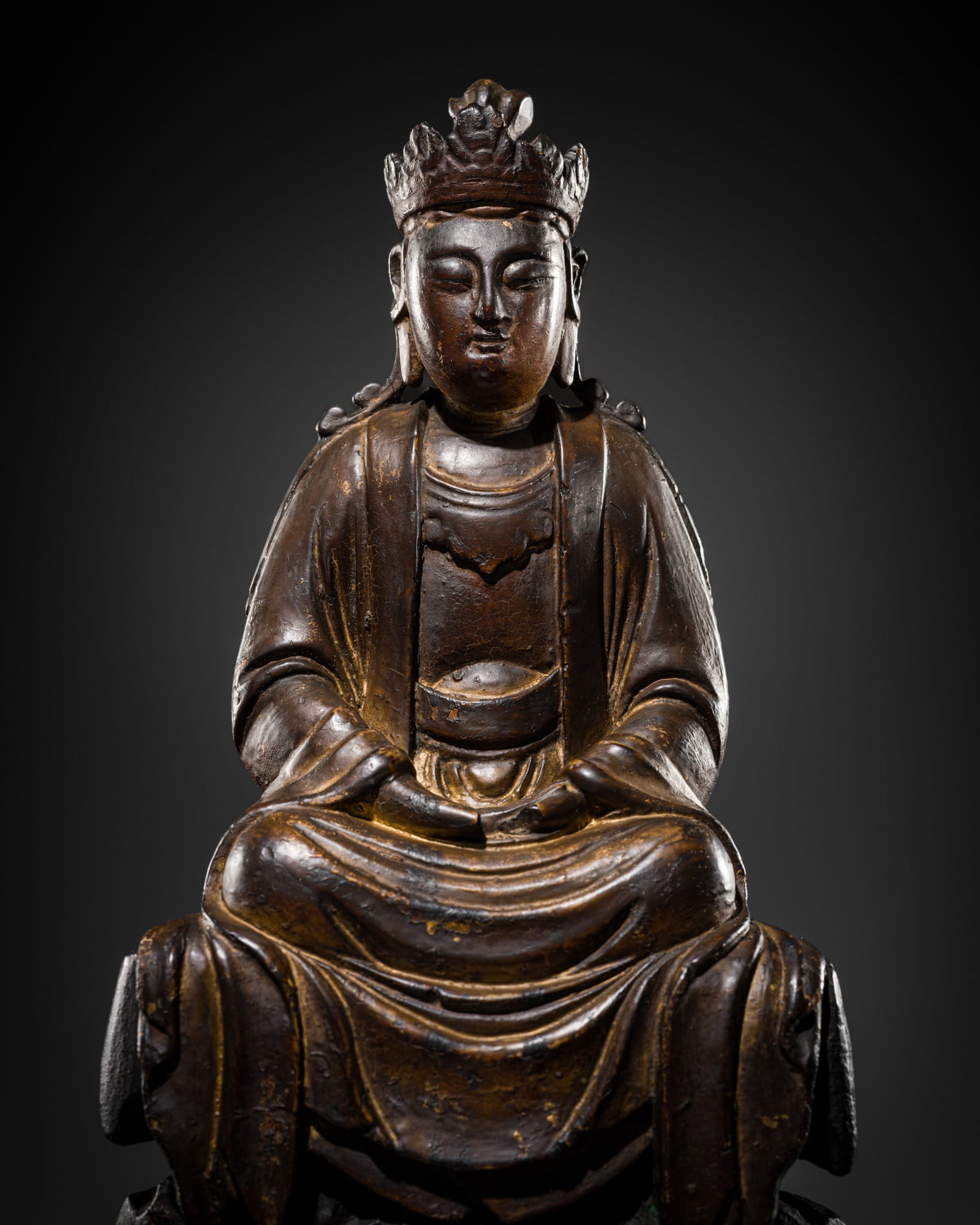 A LACQUERED WOOD FIGURE OF GUANYIN, MING DYNASTY: A LACQUERED WOOD FIGURE OF GUANYIN, MING DYNASTY China, 1368-1644. Finely carved, seated in dhyanasana, the hands lowered in dhyana mudra. The deity wears voluminous robes with intricately rendered fo
