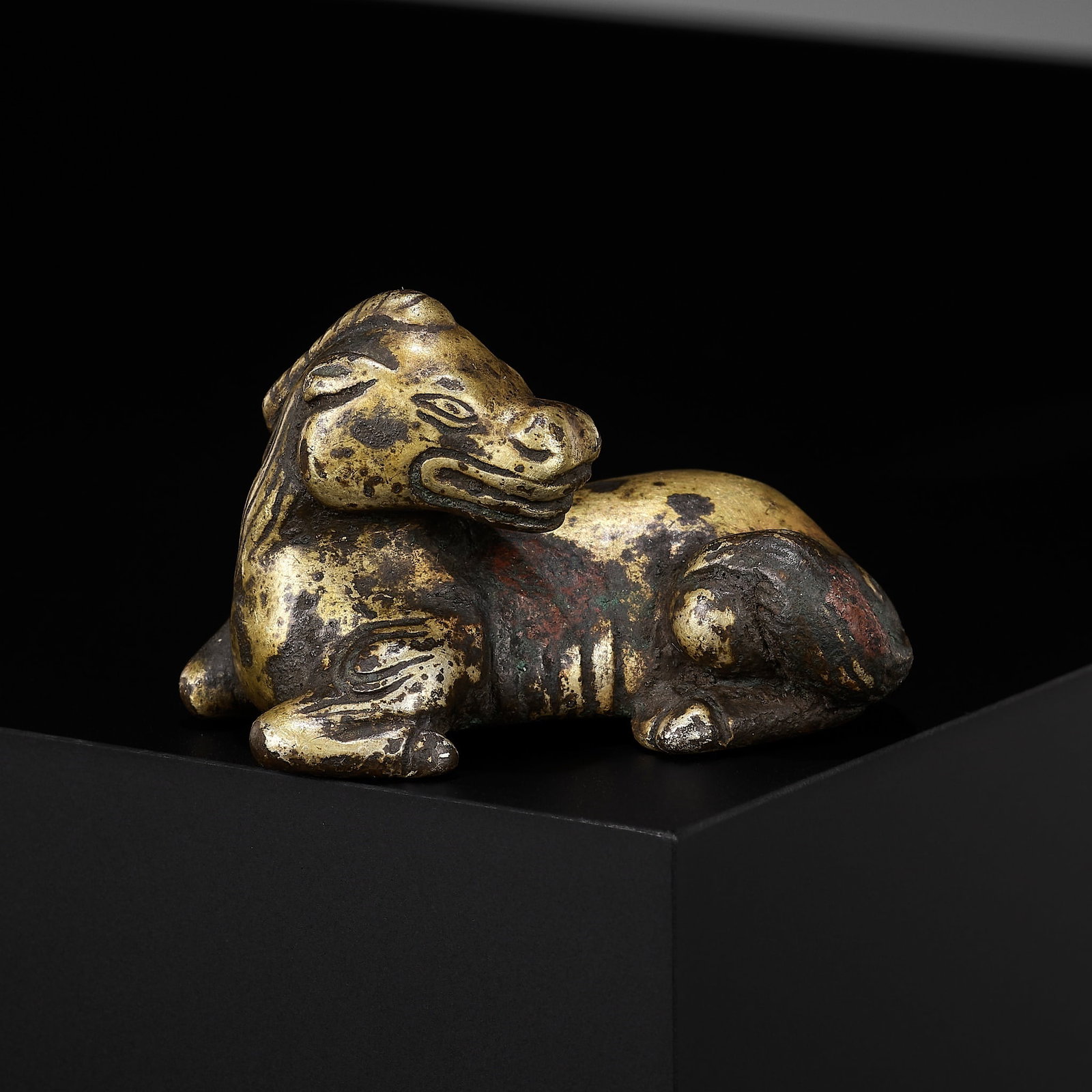 A GILT-BRONZE 'XINIU' WEIGHT, MING DYNASTY: A GILT-BRONZE 'XINIU' WEIGHT, MING DYNASTY China, 1368-1644. Finely cast, the legendary beast seated in a recumbent position with its head turned back over its body. The tail of the creature flicked a