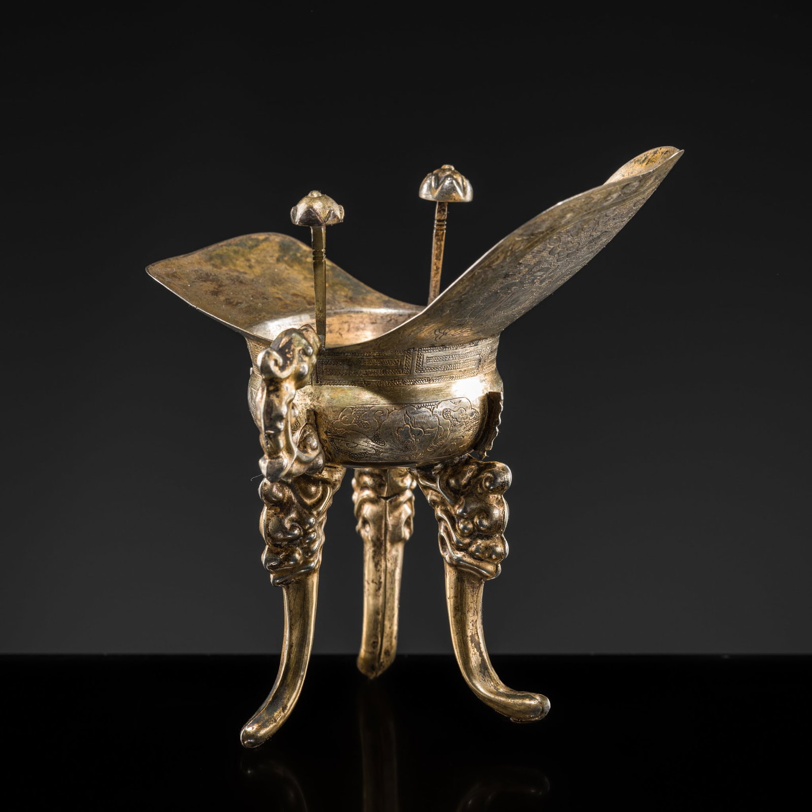 A GILT SILVER TRIPOD LIBATION CUP, JUE, 19TH CENTURY: A GILT SILVER TRIPOD LIBATION CUP, JUE, 19TH CENTURY China. The vessel supported on three long curved feet issuing from dragon heads, one side set with a dragon-form handle, with a characteristic pair