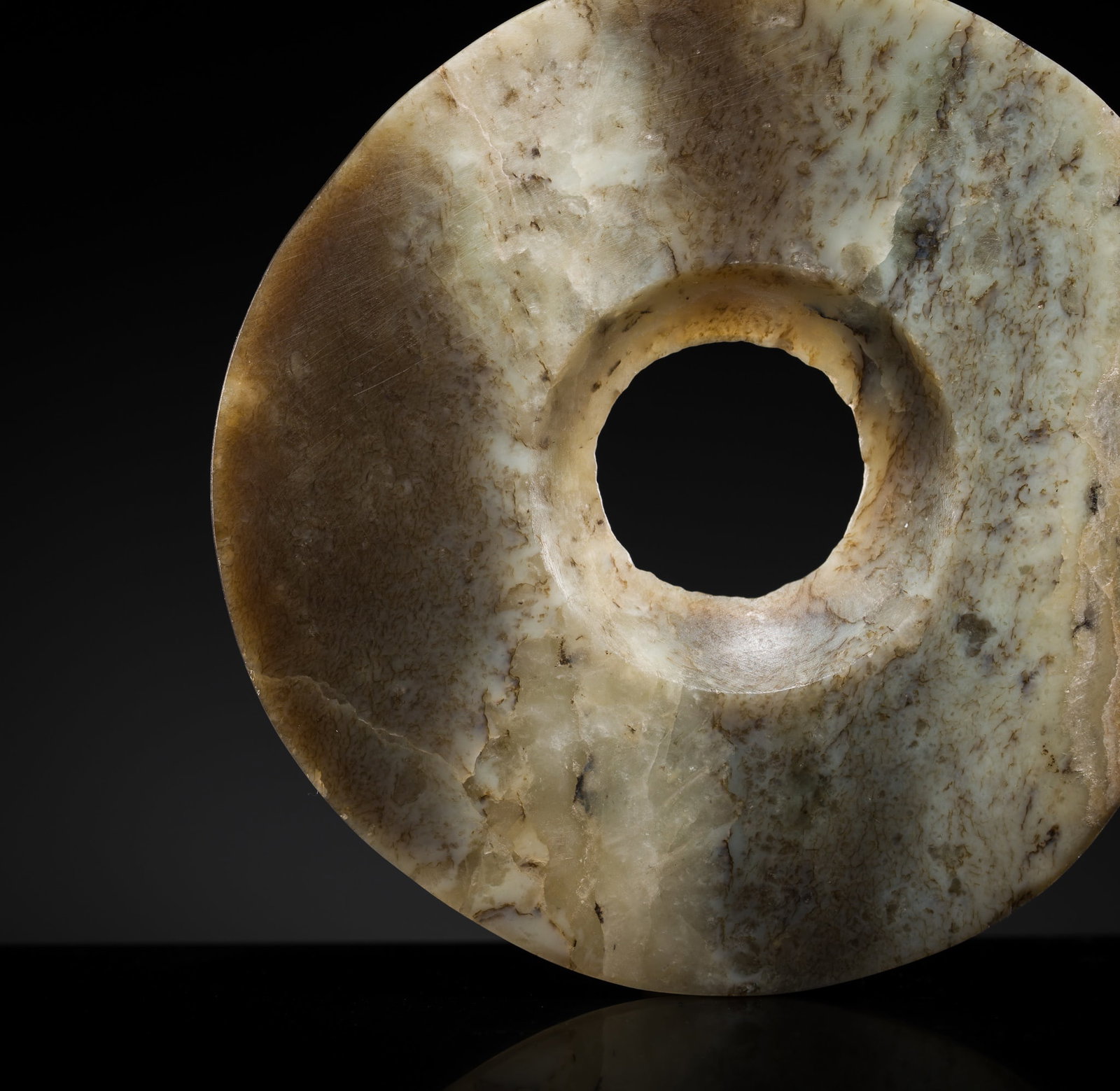 A PALE GREEN AND BROWN JADE DISC, BI, NEOLITHIC PERIOD, QIJIA CULTURE: A PALE GREEN AND BROWN JADE DISC, BI, NEOLITHIC PERIOD, QIJIA CULTURE China, circa 2300-1500 BC. The circular disk with flat sides and pierced from one side with a central aperture. The semi-transluce