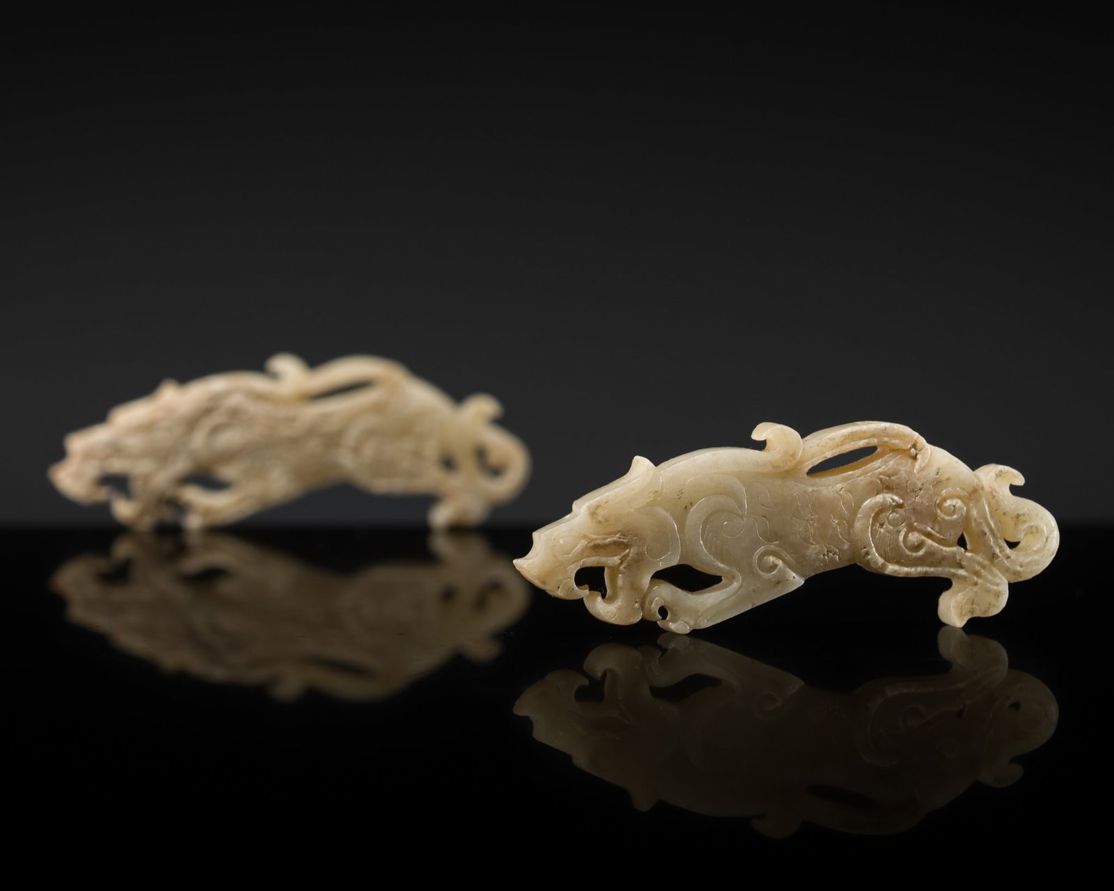 A RARE PAIR OF MINIATURE WHITE JADE 'TIGER' PENDANTS, EASTERN ZHOU DYNASTY: A RARE PAIR OF MINIATURE WHITE JADE 'TIGER' PENDANTS, EASTERN ZHOU DYNASTY China, 770-221 BC. Each finely carved in openwork as a recumbent tiger in profile, the slender body, gracefully arched and de