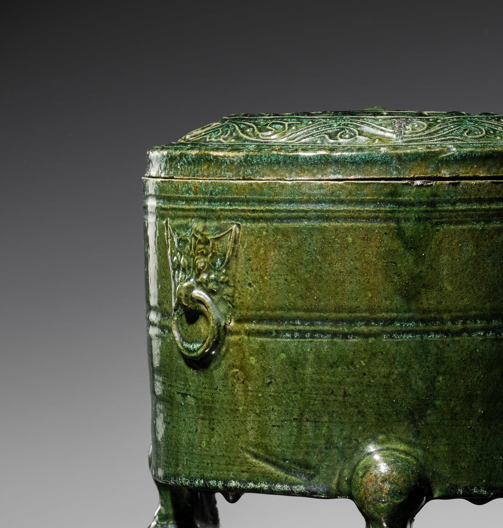 A GREEN-GLAZED POTTERY TRIPOD JAR AND COVER, LIAN, HAN DYNASTY: A GREEN-GLAZED POTTERY TRIPOD JAR AND COVER, LIAN, HAN DYNASTY China, 206 BC-220 AD. The cylindrical body raised on three cabriole feet, set with a pair of taotie mask handles suspending mock-rings, a