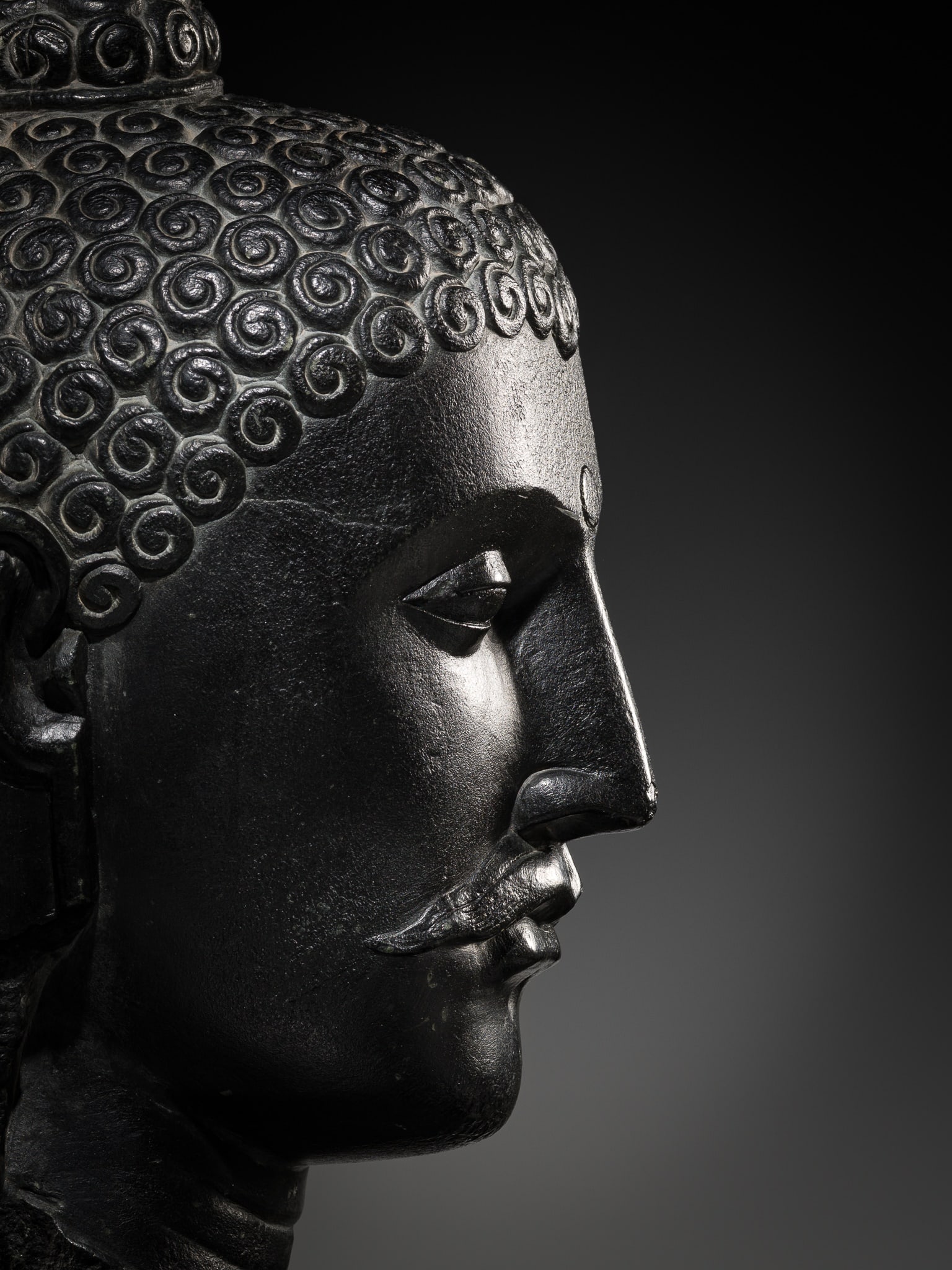 A RARE AND MONUMENTAL BLACK STONE HEAD OF BUDDHA, EARLY PALA PERIOD, CIRCA 7TH-8TH CENTURY: A RARE AND MONUMENTAL BLACK STONE HEAD OF BUDDHA, EARLY PALA PERIOD, CIRCA 7TH-8TH CENTURY India. Superbly carved, the face with a serene, meditative expression marked by heavy-lidded downcast eyes wi