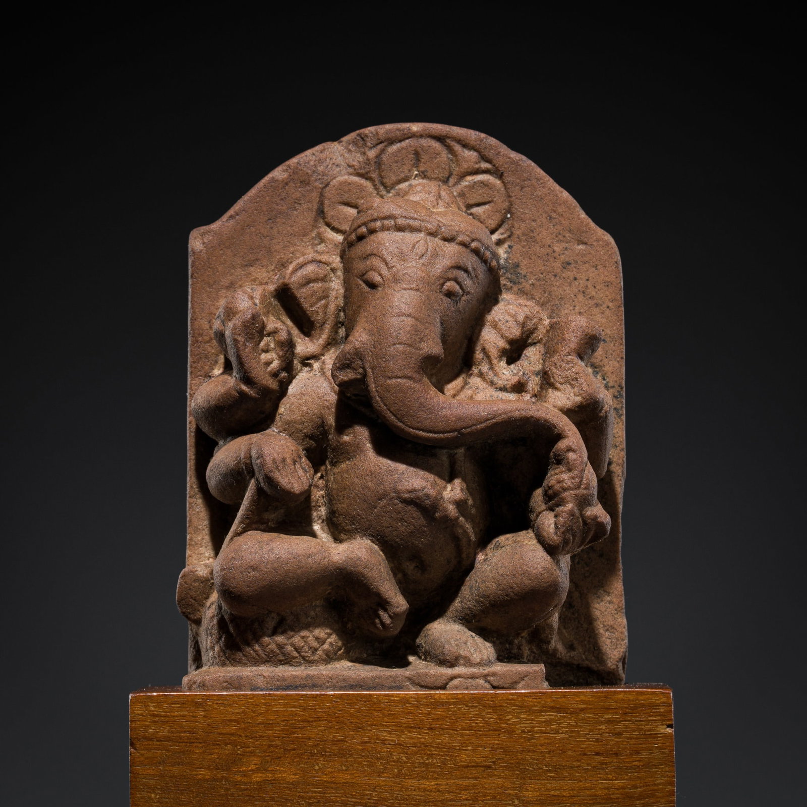 A SMALL RED SANDSTONE FIGURE OF GANESHA, MAHARASHTRA, 8TH-9TH CENTURY: A SMALL RED SANDSTONE FIGURE OF GANESHA, MAHARASHTRA, 8TH-9TH CENTURY Finely carved, the potbellied deity seated atop a pedestal with legs flexed, holding a modak (sweet) in his lowered left hand, as 