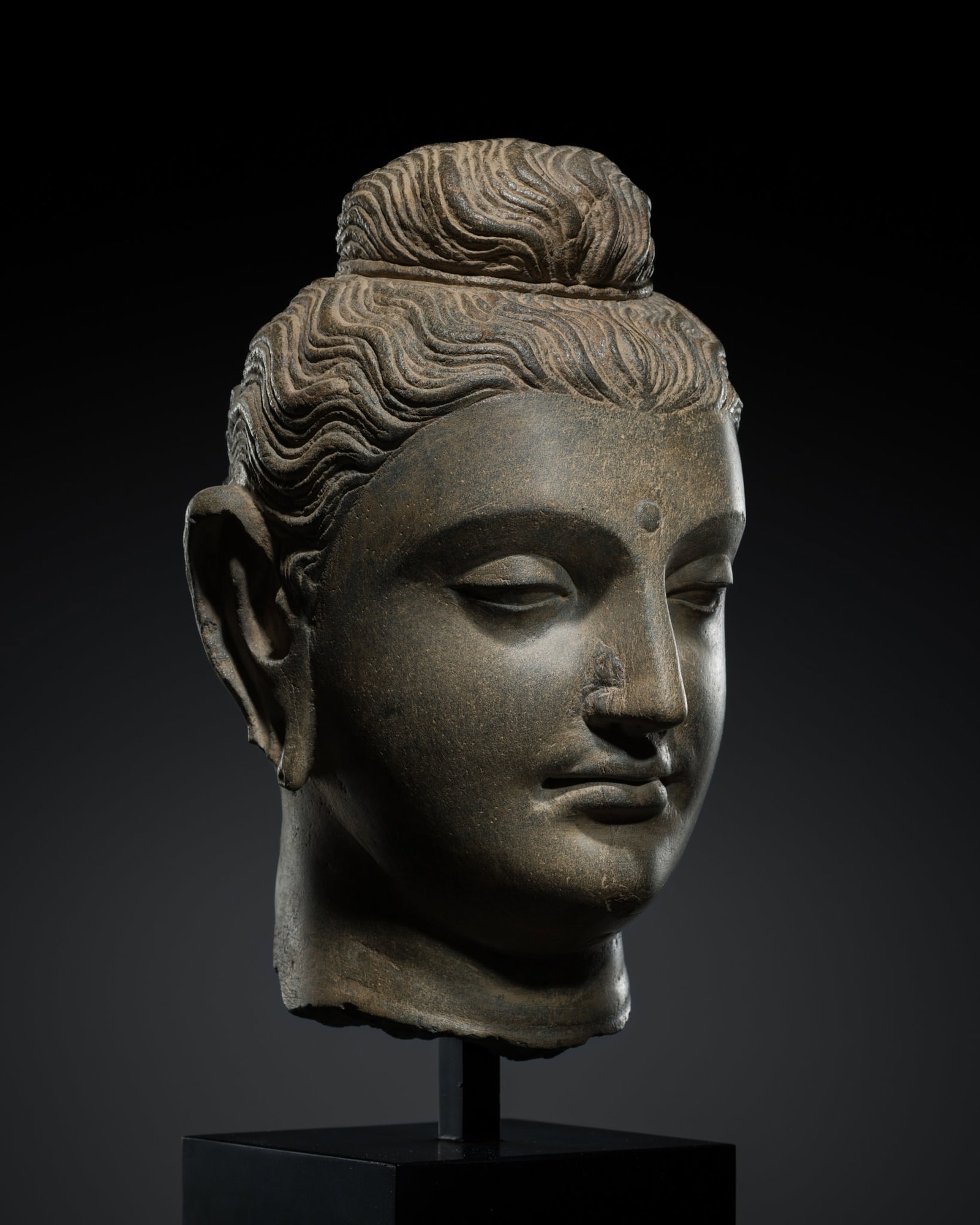 A GRAY SCHIST HEAD OF BUDDHA, ANCIENT REGION OF GANDHARA, 2ND-3RD CENTURY: A GRAY SCHIST HEAD OF BUDDHA, ANCIENT REGION OF GANDHARA, 2ND-3RD CENTURY Kushan period. Finely carved, the serene face with heavy-lidded almond-shaped eyes below elegantly arched brows, centered by a