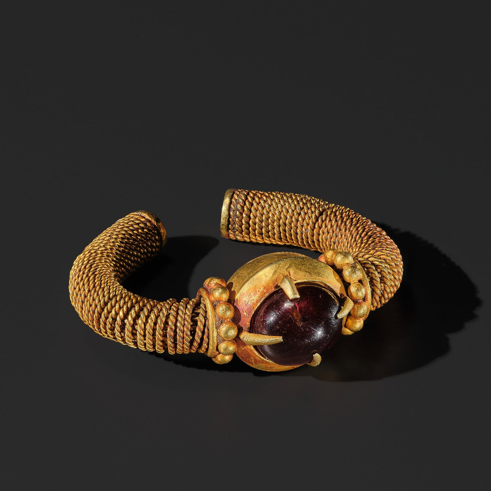 A RUBY-INSET GOLD RING, EAST JAVA, CIRCA 6TH-10TH CENTURY: A RUBY-INSET GOLD RING, EAST JAVA, CIRCA 6TH-10TH CENTURY Indonesia. The central ruby is secured by four claws rising from the globular body, flanked by gold granules at the junctions, the curved side