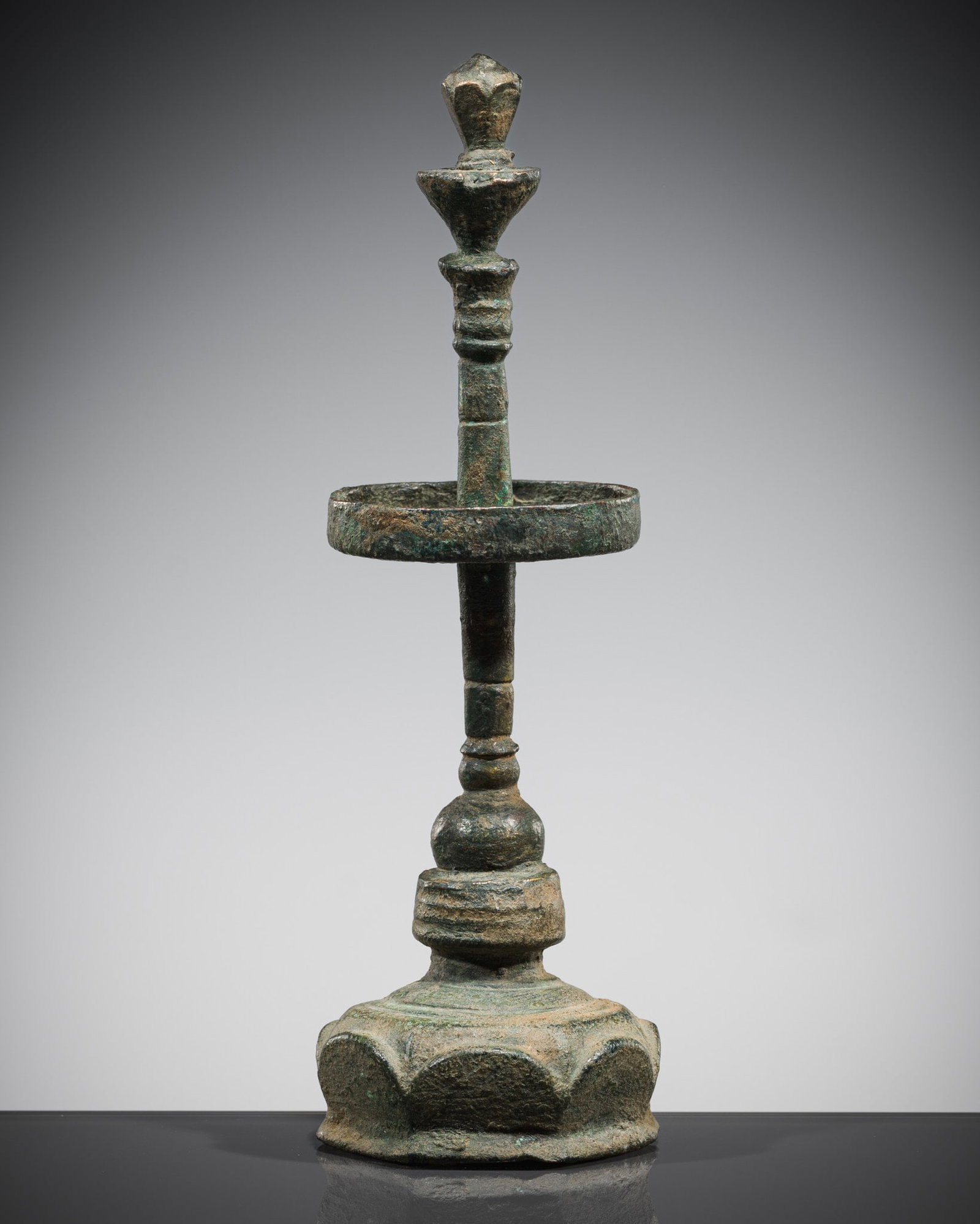 A BRONZE OIL LAMP, ANGKOR PERIOD, 12TH-13TH CENTURY: A BRONZE OIL LAMP, ANGKOR PERIOD, 12TH-13TH CENTURY Khmer Empire. The shallow oil reservoir is circular in form, surmounted by a tall, ribbed stem with a flared finial in the form of a lotus bud, the 