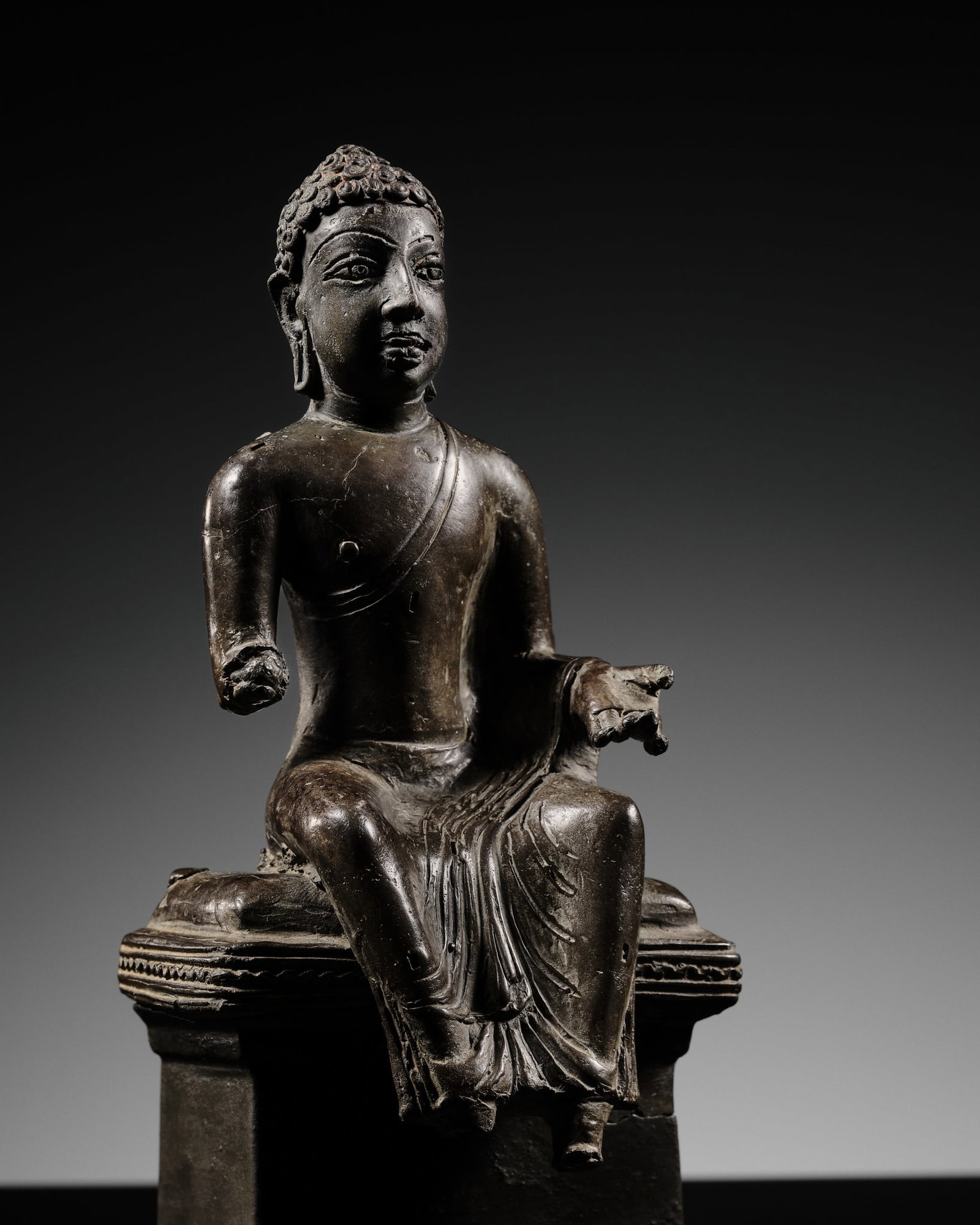 A SILVERED COPPER ALLOY FIGURE OF THE ENTHRONED BUDDHA, MON-DVARAVATI, THAILAND, 8TH-9TH CENTURY: A SILVERED COPPER ALLOY FIGURE OF THE ENTHRONED BUDDHA, MON-DVARAVATI, THAILAND, 8TH-9TH CENTURY Finely cast seated in bhadrasana atop a cushioned pedestal decorated with a sawtooth rim, his extended 