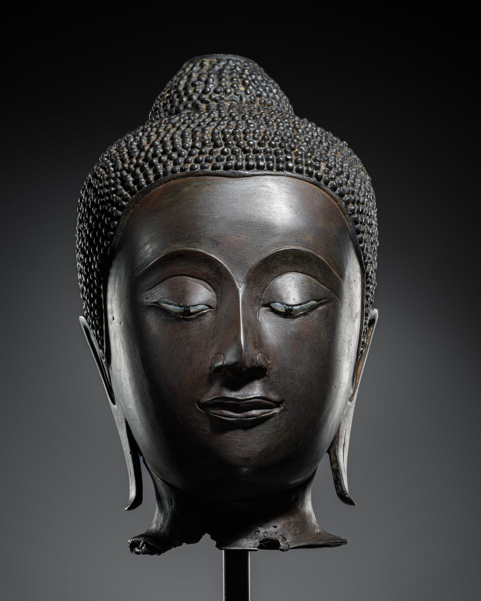 A BRONZE HEAD OF BUDDHA, AYUTTHAYA PERIOD, 16TH-17TH CENTURY: A BRONZE HEAD OF BUDDHA, AYUTTHAYA PERIOD, 16TH-17TH CENTURY Superbly cast, the oval face with a serene expression, the heavy-lidded downcast eyes neatly inlaid with mother-of-pearl with black lacquer