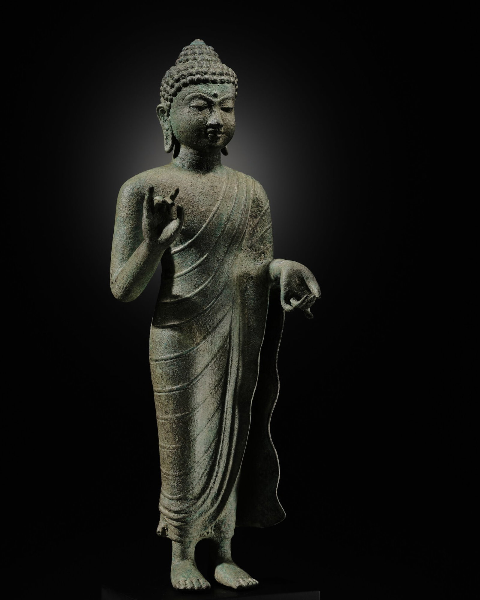 A BRONZE FIGURE OF BUDDHA, SRIVIJAYA, 8TH-9TH CENTURY: † A BRONZE FIGURE OF BUDDHA, SRIVIJAYA, 8TH-9TH CENTURY Western Indonesia. Finely cast standing in samapada, the right hand raised in abhaya mudra while the left hand is lowered in vitarka mudra