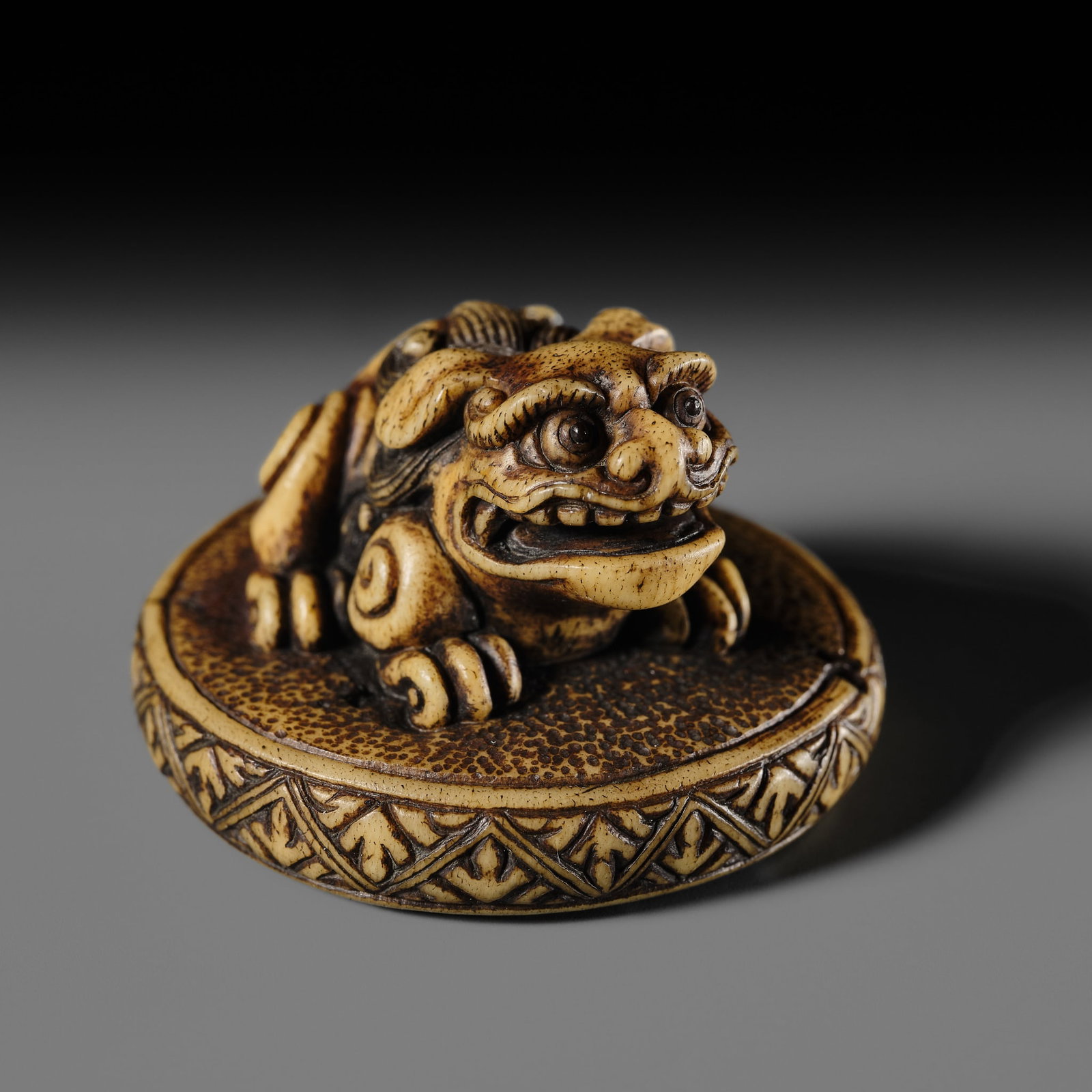 A FINE ANTLER NETSUKE OF A SHISHI ON A CUSHION, ATTRIBUTED TO RENSAI: A FINE ANTLER NETSUKE OF A SHISHI ON A CUSHION, ATTRIBUTED TO RENSAI Attributed to Ishikawa Rensai, unsigned Japan, Tokyo, Asakusa district, second half of the 19th century Finely carved from a heavil