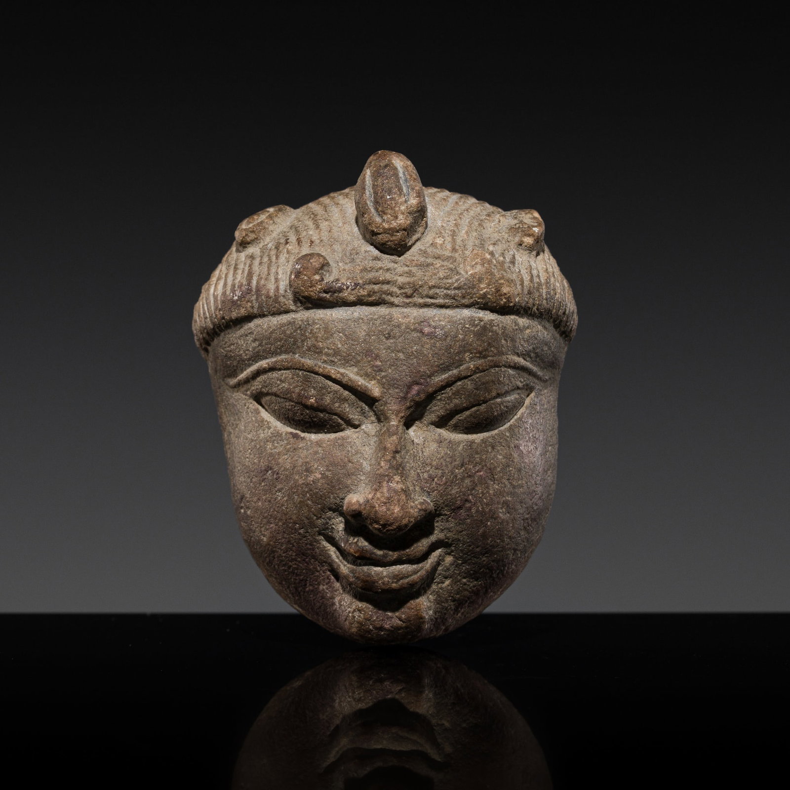 A CENTRAL INDIAN MINIATURE STONE HEAD OF A DEITY: A CENTRAL INDIAN MINIATURE STONE HEAD OF A DEITY This lot is from a single owner collection and is therefore offered without reserve 11th-12th century. The oval face with rounded cheeks, almond shaped