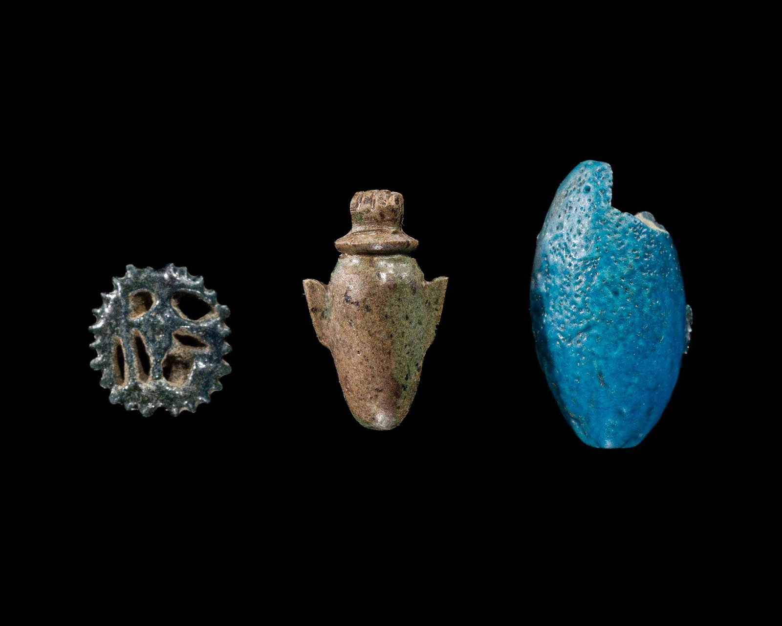 A GROUP OF THREE FAIENCE AND STONE AMULWITH A BLUE-GLAZED FAIENCE 'UREAUS HEAD' SEAL AND A GREEN: A GROUP OF THREE FAIENCE AND STONE AMULWITH A BLUE-GLAZED FAIENCE 'UREAUS HEAD' SEAL AND A GREEN STONE 'HEART' AND 'WEDJAT EYE' MINIATURE AMULETS, NEW KINGDOM TO THIRD INTERMEDIATE PERIOD This lot is 
