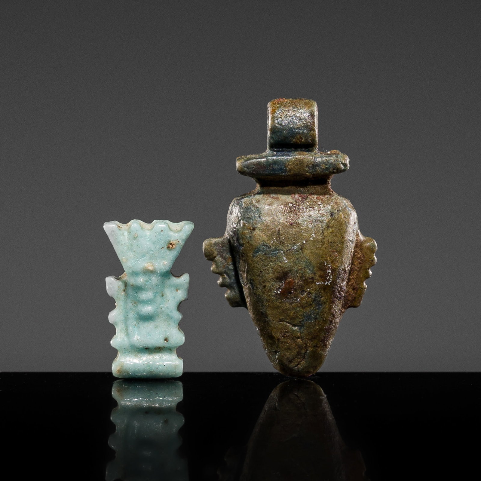 A PALE BLUE FAIENCE 'BES' AMULET AND A DARK GREEN STONE 'HEART' AMULET, LATE PERIOD-PTOLEMAIC PERIOD: A PALE BLUE FAIENCE 'BES' AMULET AND A DARK GREEN STONE 'HEART' AMULET, LATE PERIOD-PTOLEMAIC PERIOD This lot is from a single owner collection and is therefore offered without reserve The Jorgen Rube