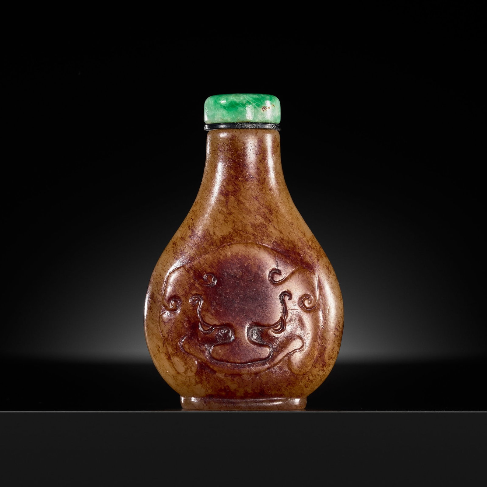 A RUSSET AND BEIGE JADE 'TAOTIE MASKS' SNUFF BOTTLE, 1780-1840: A RUSSET AND BEIGE JADE 'TAOTIE MASKS' SNUFF BOTTLE, 1780-1840 China. Well hollowed, of pear form, supported on an oval foot and rising to a long neck with flat lip, the wider sides carved in low reli