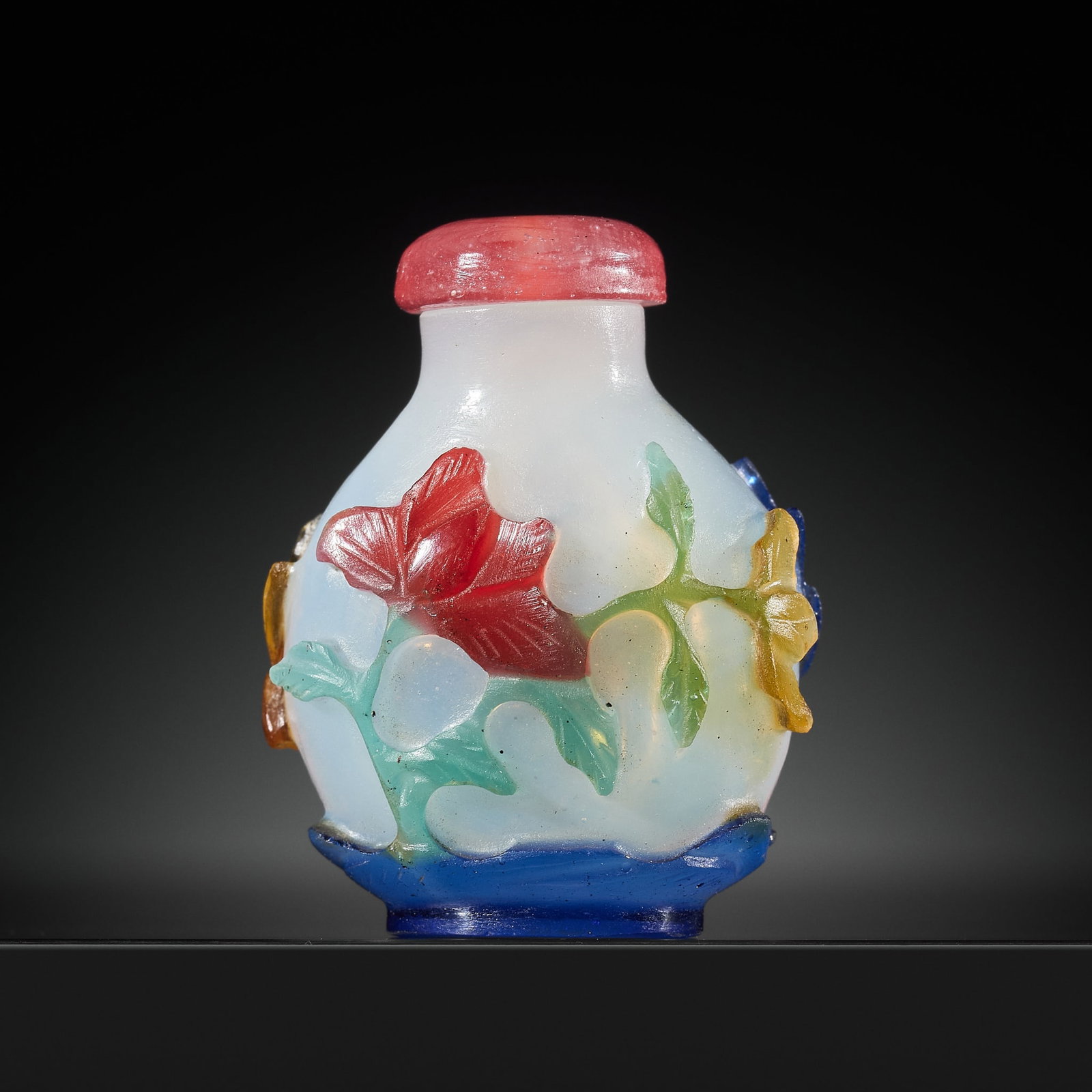 A FOUR-COLOR OVERLAY 'LOTUS AND BUTTERFLIES' MILKY GLASS SNUFF BOTTLE, 19TH CENTURY: A FOUR-COLOR OVERLAY 'LOTUS AND BUTTERFLIES' MILKY GLASS SNUFF BOTTLE, 19TH CENTURY China. Of ovoid form rising from an oval foot to a short cylindrical neck with flat mouth, carved through the pale g