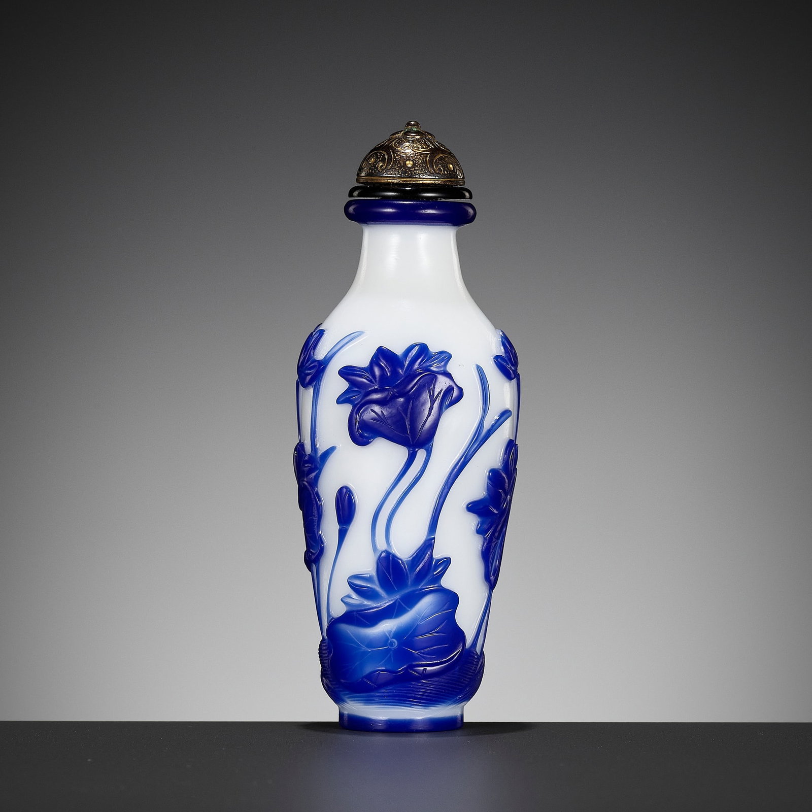 A SAPPHIRE-BLUE GLASS OVERLAY 'LOTUS POND' SNUFF BOTTLE, ATTRIBUTED TO THE IMPERIAL GLASSWORKS,: A SAPPHIRE-BLUE GLASS OVERLAY 'LOTUS POND' SNUFF BOTTLE, ATTRIBUTED TO THE IMPERIAL GLASSWORKS, BEIJING, 1750-1790 The baluster body supported on a short foot and rising to a rounded shoulder with tap